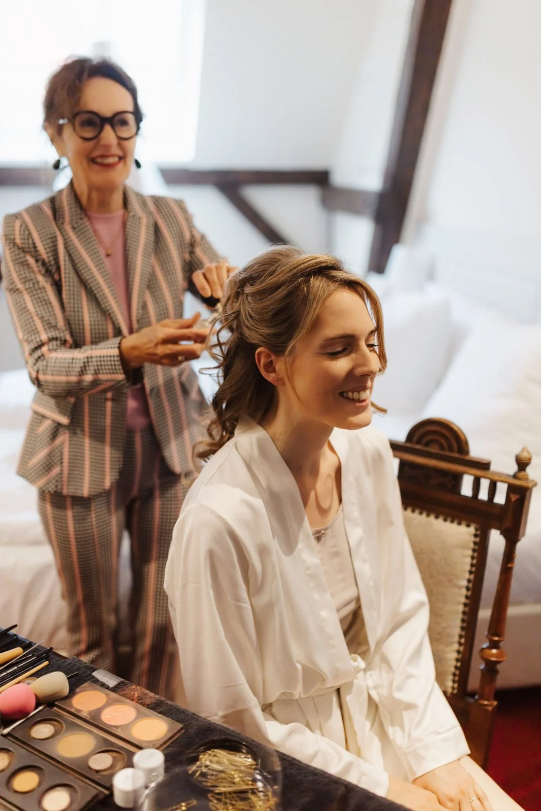 Lachende Braut im weißen Morgenmantel beim Getting Ready, während ihre Hochzeitsfrisur gestylt wird – natürliche Hochzeitsreportage im Heide Hotel Reinstorf bei Lüneburg.