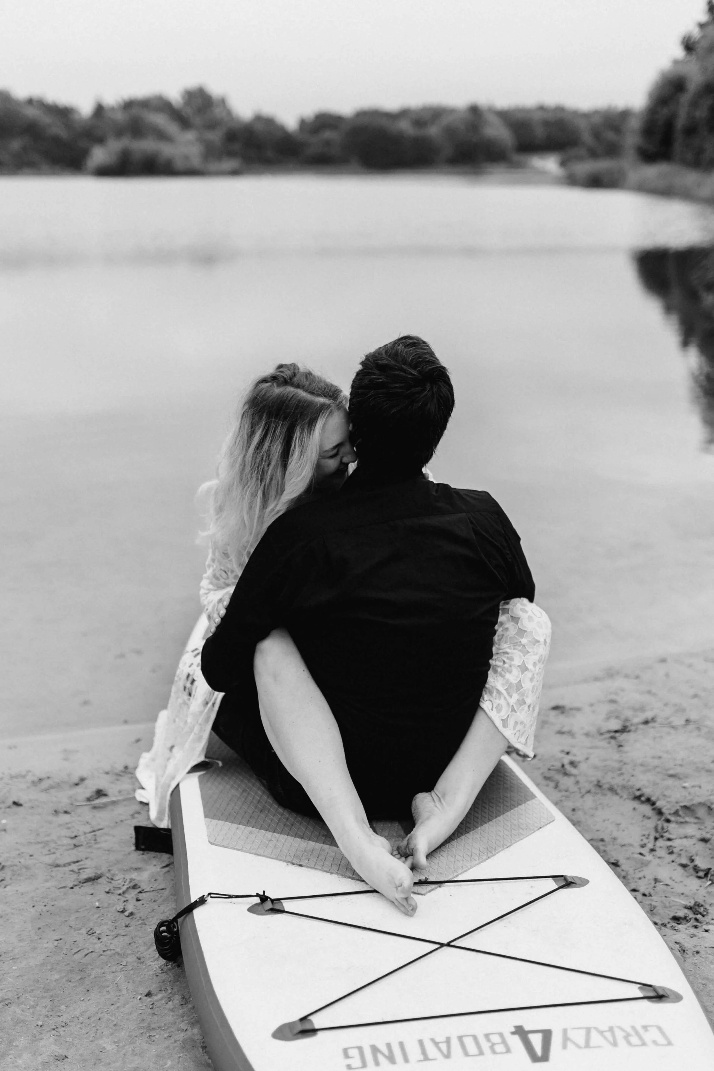 Paar sitzt eng umschlungen auf einem SUP und blickt gemeinsam über den See in einem Schwarz-Weiß-Foto