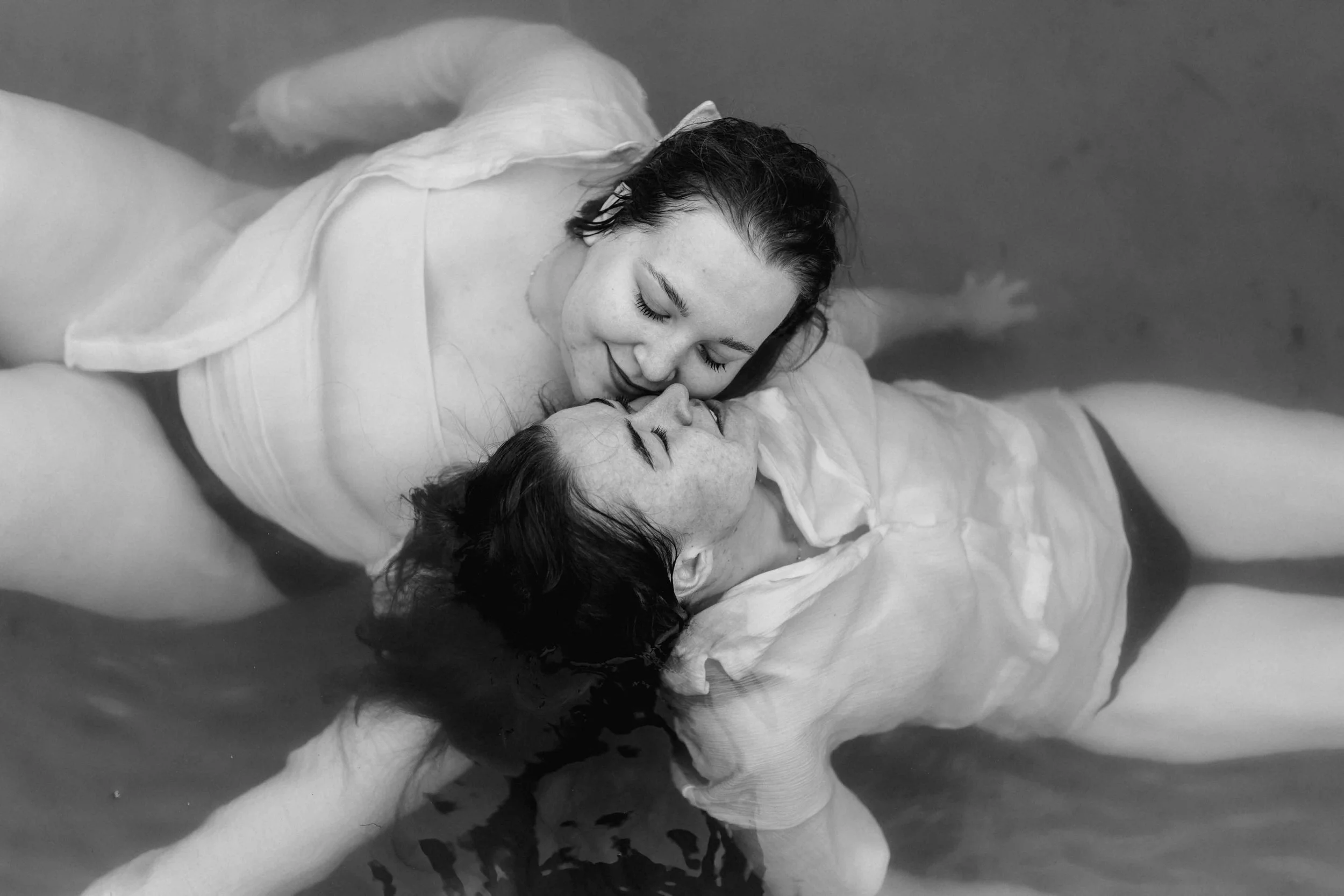 Zwei Frauen treiben umschlungen im Wasser und lächeln sich zärtlich an, Schwarz-Weiß-Fotografie