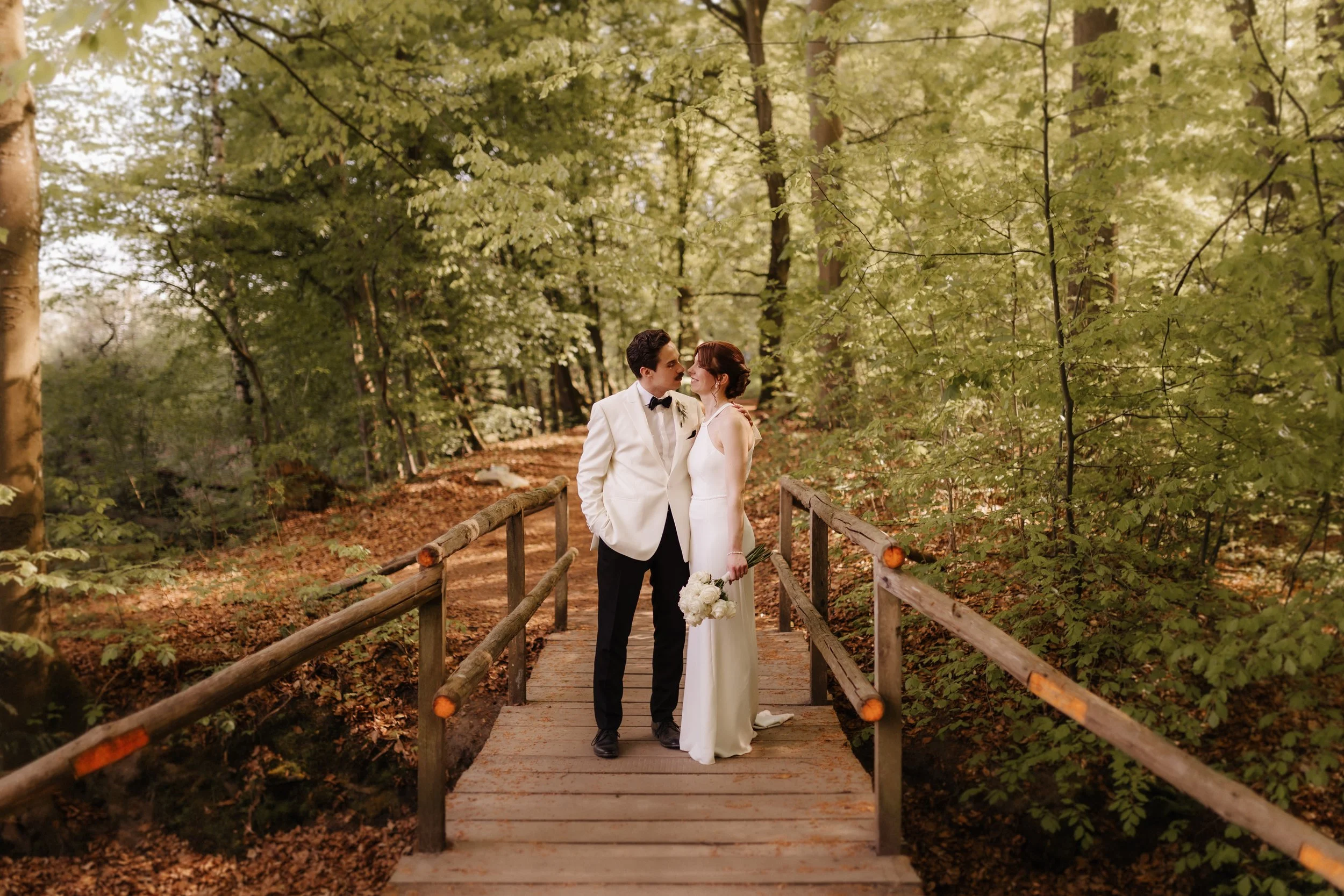 Brautpaar küsst sich auf einer kleinen Holzbrücke mitten im grünen Wald beim romantischen Hochzeitsshooting am Forsthaus Rote Schleuse in Lüneburg.
