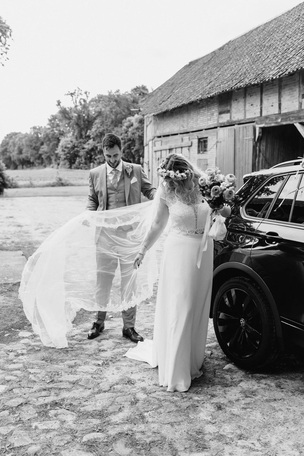 Brautpaar mit Schleier vor dem Hochzeitsauto auf einem Hof bei Lüneburg