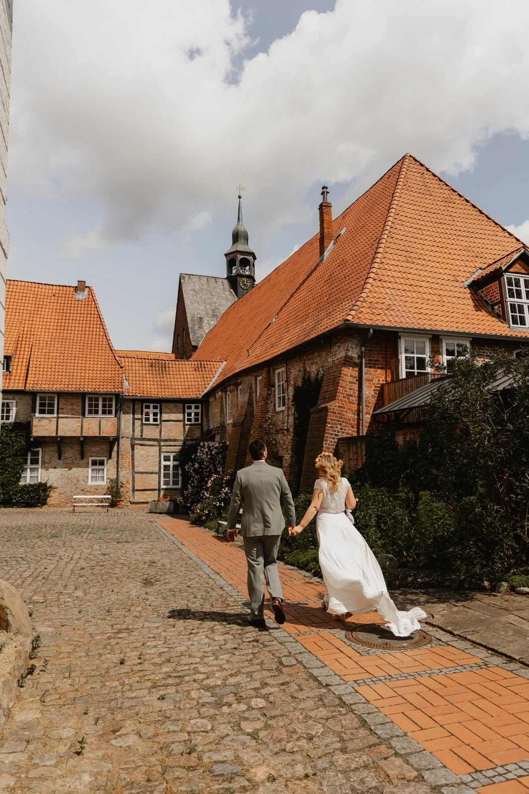 Brautpaar spaziert Hand in Hand durch die Altstadt von Lüneburg mit Blick auf das historische Rathaus
