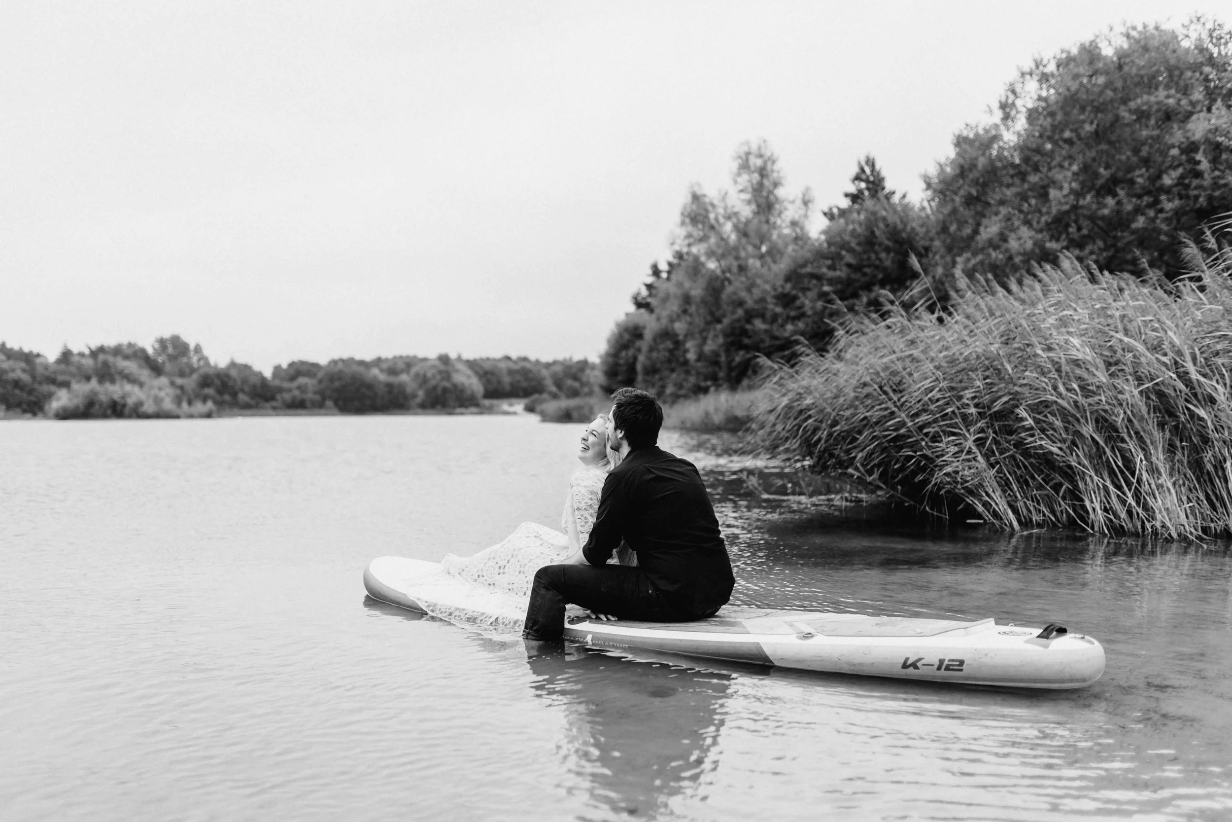 Paar sitzt auf einem SUP-Board am See und schaut gemeinsam in die Ferne, schwarz weiß Fotografie