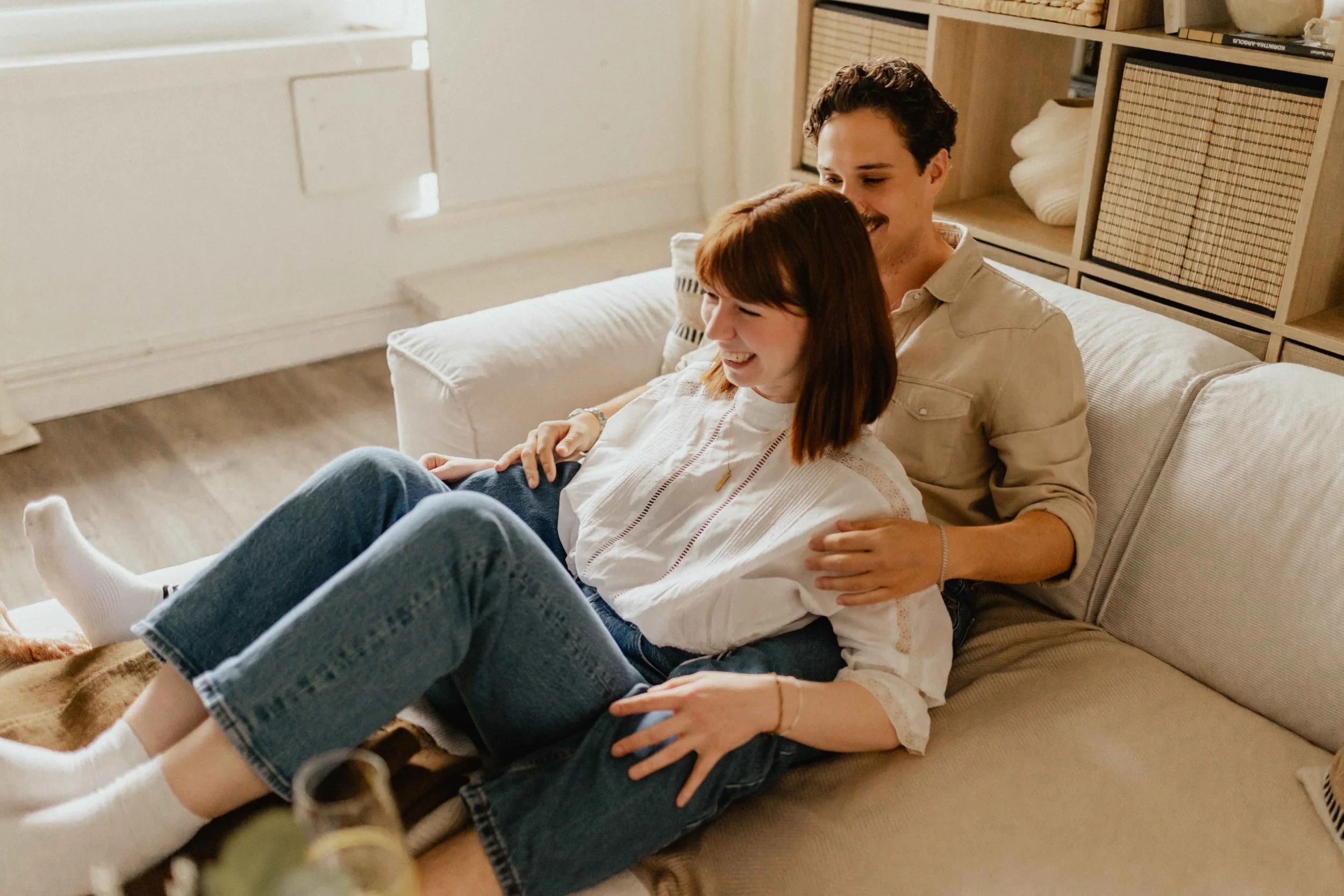 Paar bei einer Homestory in Lüneburg sitzt entspannt auf dem Sofa, er legt den Arm um sie und beide lachen miteinander