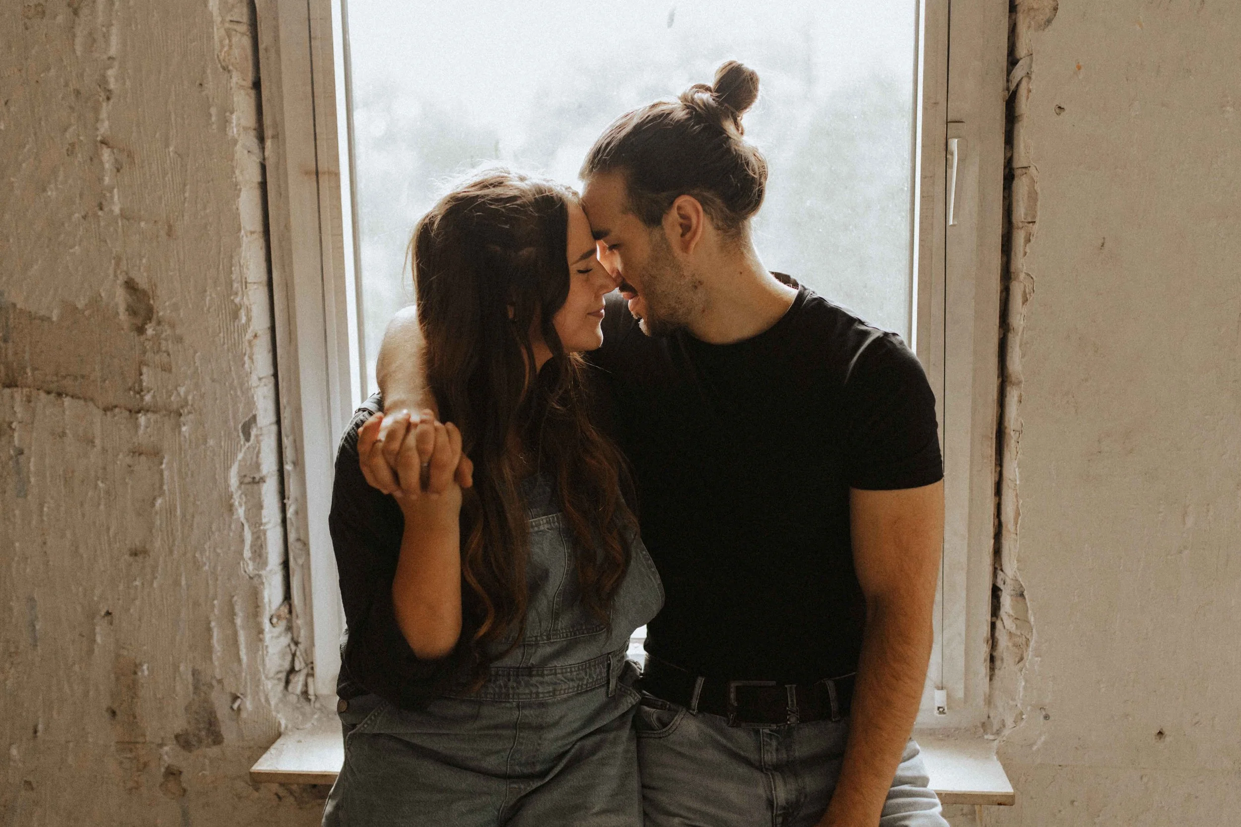 Paarshooting auf Baustelle – verliebtes Paar sitzt eng beieinander auf einer Fensterbank, Stirn an Stirn, und hält sich liebevoll an den Händen in Lüneburg.