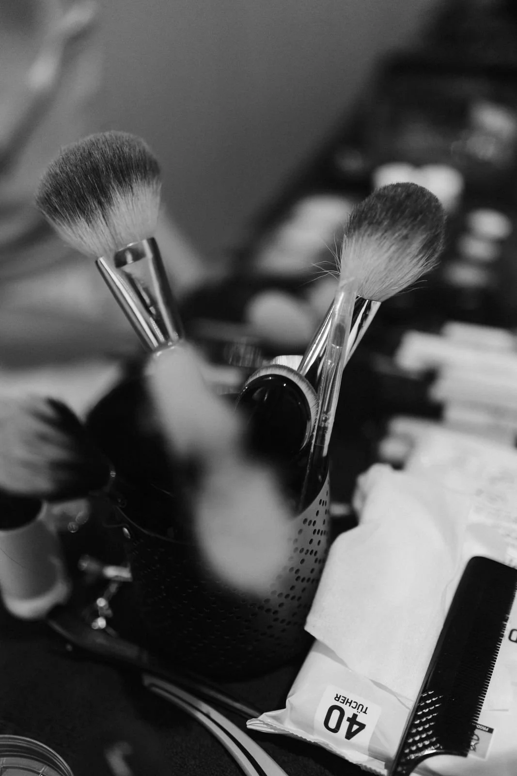 Schwarz-Weiß-Aufnahme von Make-up-Pinseln, Schminkutensilien und Kosmetikprodukten beim Getting Ready der Braut für ihre Hochzeit im Heide Hotel Reinstorf bei Lüneburg.