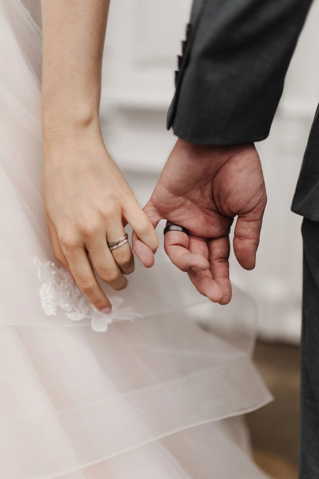 Romantische Detailaufnahme der Hände von Braut und Bräutigam mit Eheringen, während sie ihre kleinen Finger ineinanderhaken. Hochzeitsfotografie beim Brautpaarshooting im Heide Hotel Reinstorf bei Lüneburg.