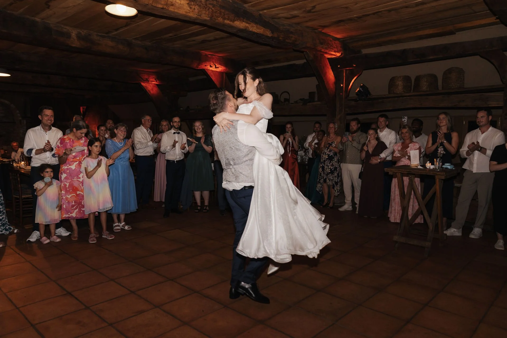 Bräutigam hebt die Braut beim Hochzeitstanz hoch, während die Hochzeitsgäste das Paar auf der Tanzfläche umringen