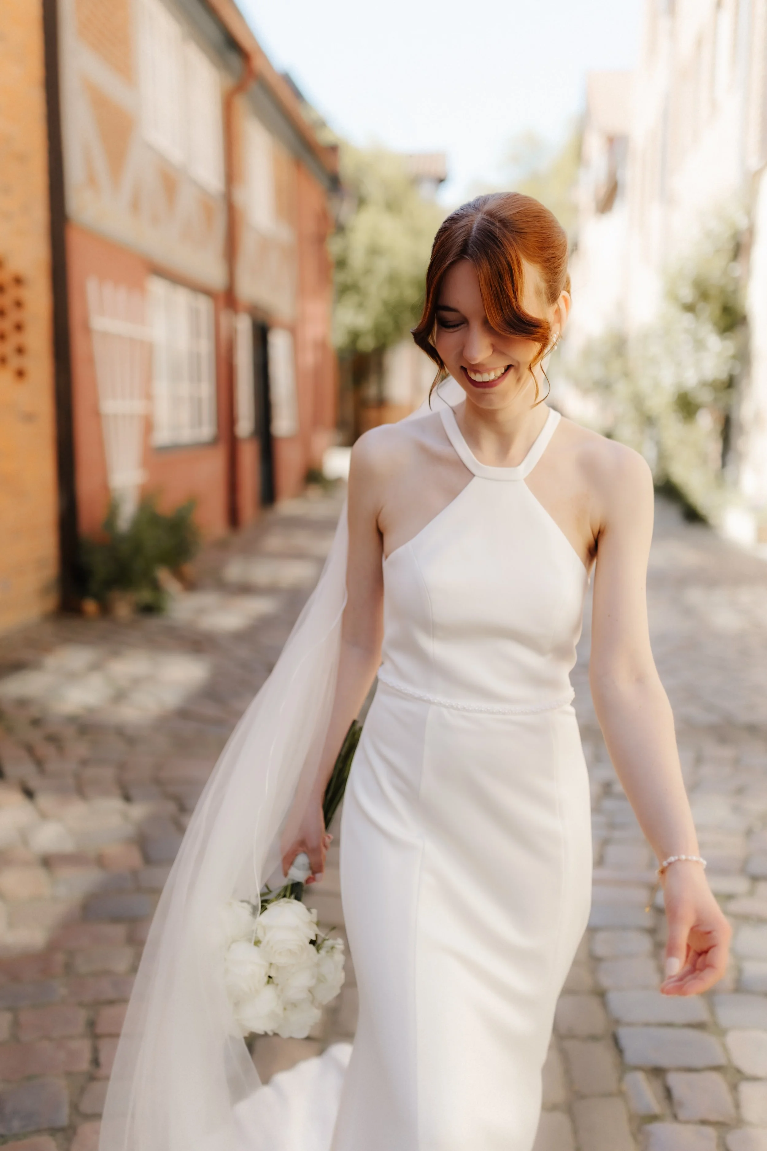 Strahlende Braut im modernen Brautkleid mit weißem Brautstrauß in der historischen Lüneburger Altstadt.