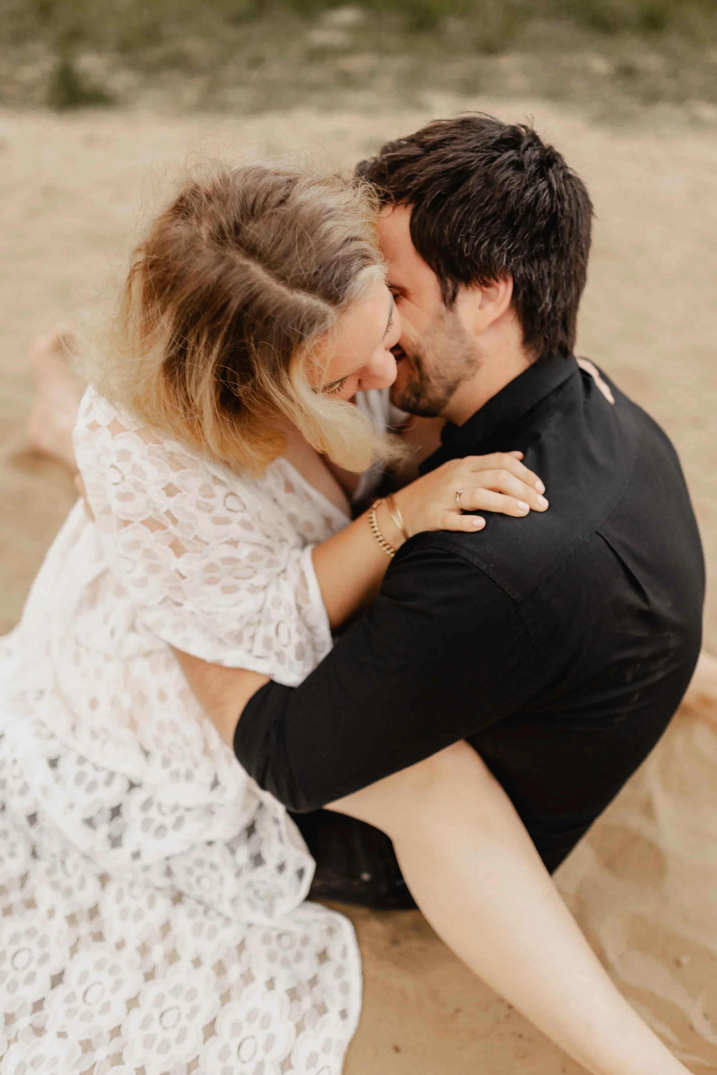 Paar sitzt eng umschlungen am Sandufer und küsst sich leidenschaftlich