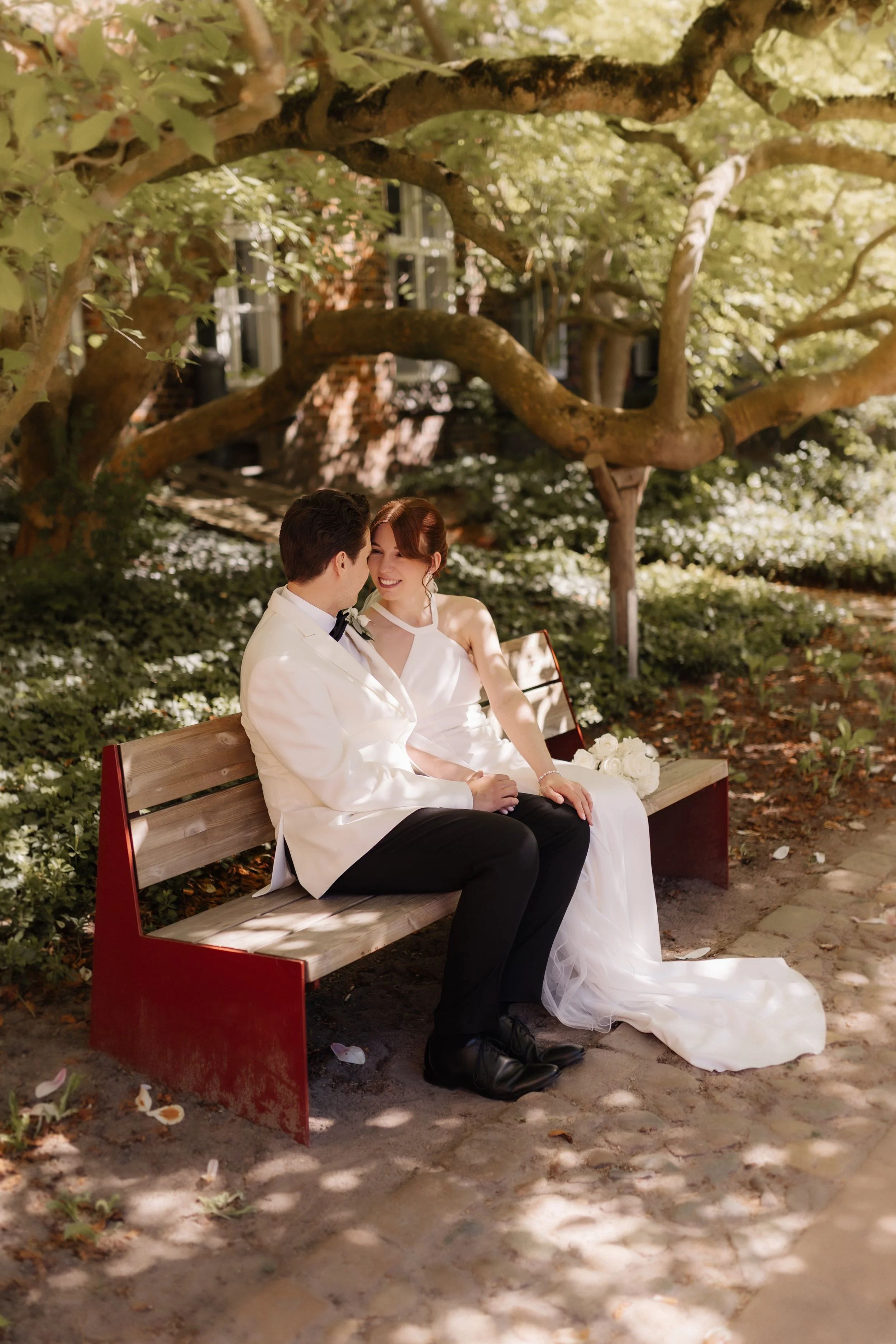 Brautpaar sitzt nach der Hochzeit gemeinsam auf einer Bank unter einem großen Baum im Rathausgarten in Lüneburg.