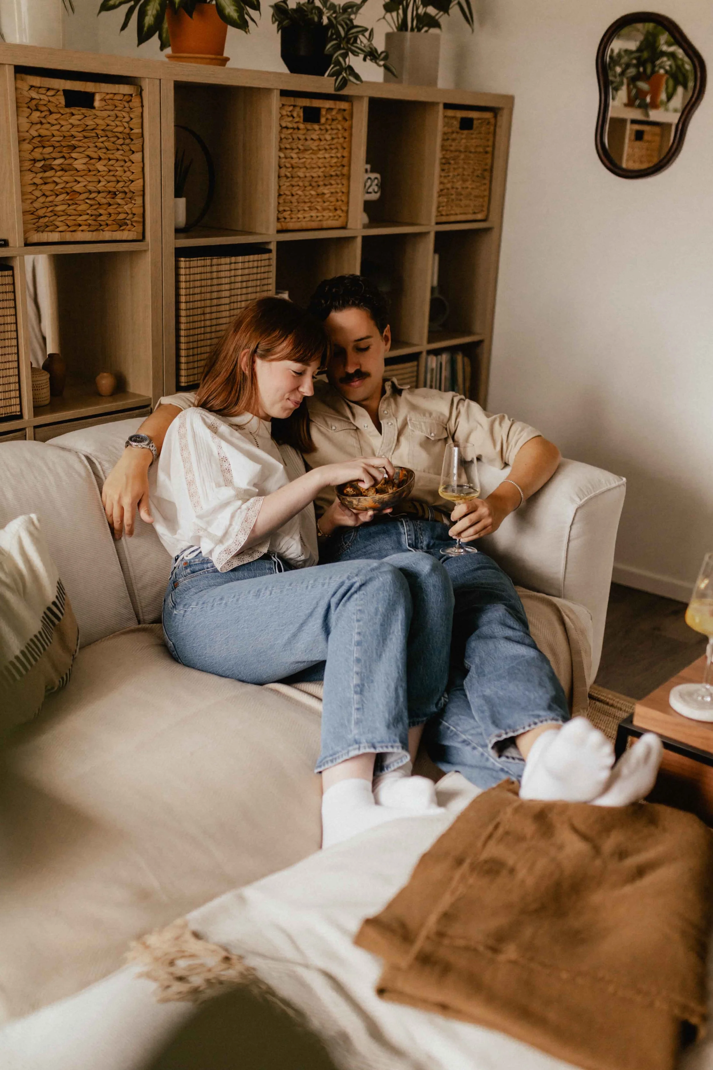 Paar sitzt bei einer Homestory in Lüneburg eng beisammen auf dem Sofa, teilt Gebäck und Wein in gemütlicher Atmosphäre