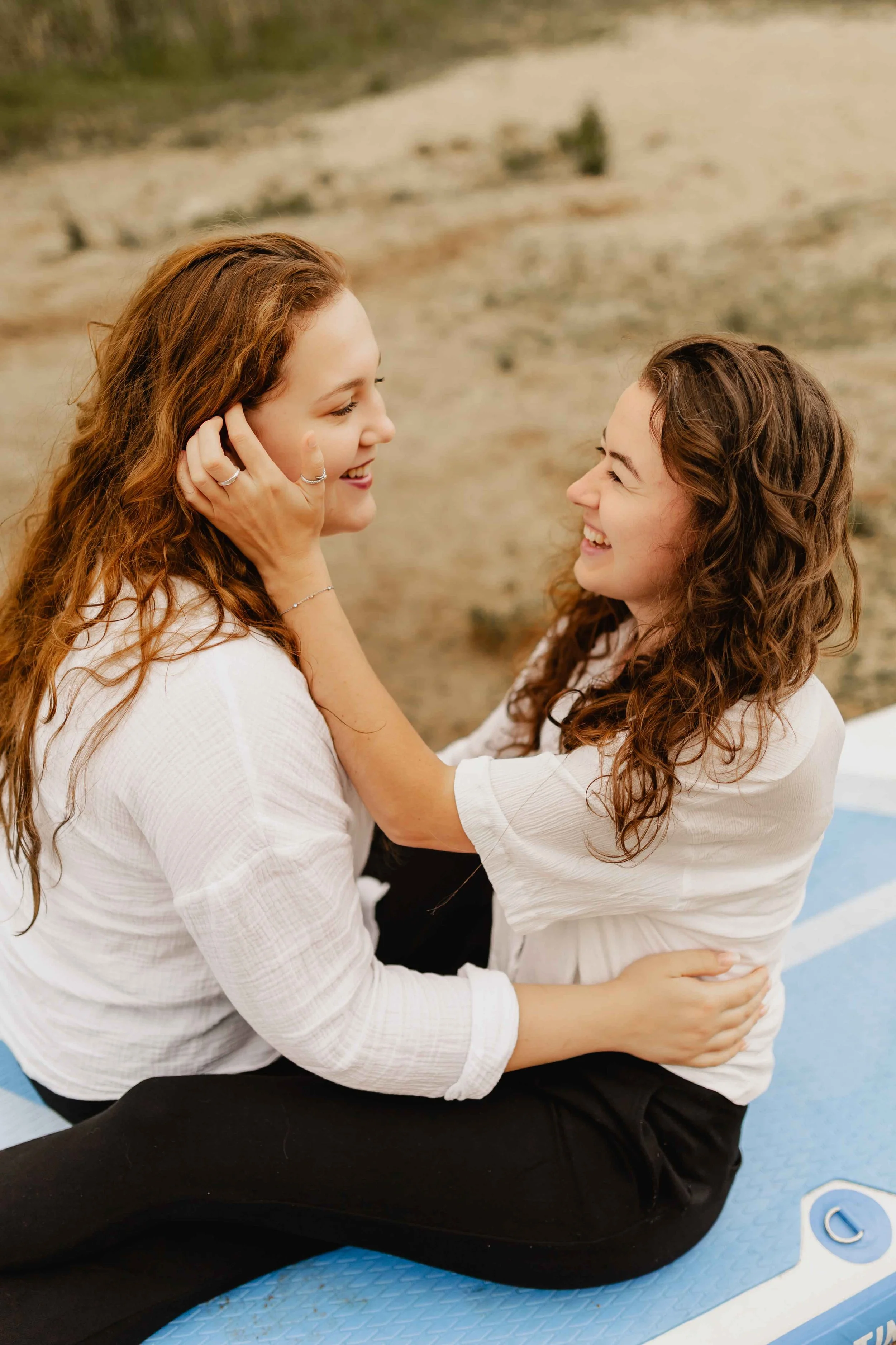 Zwei Frauen sitzen auf einem SUP-Board am Oldenstädter See, schauen sich an und halten sich zärtlich im Arm