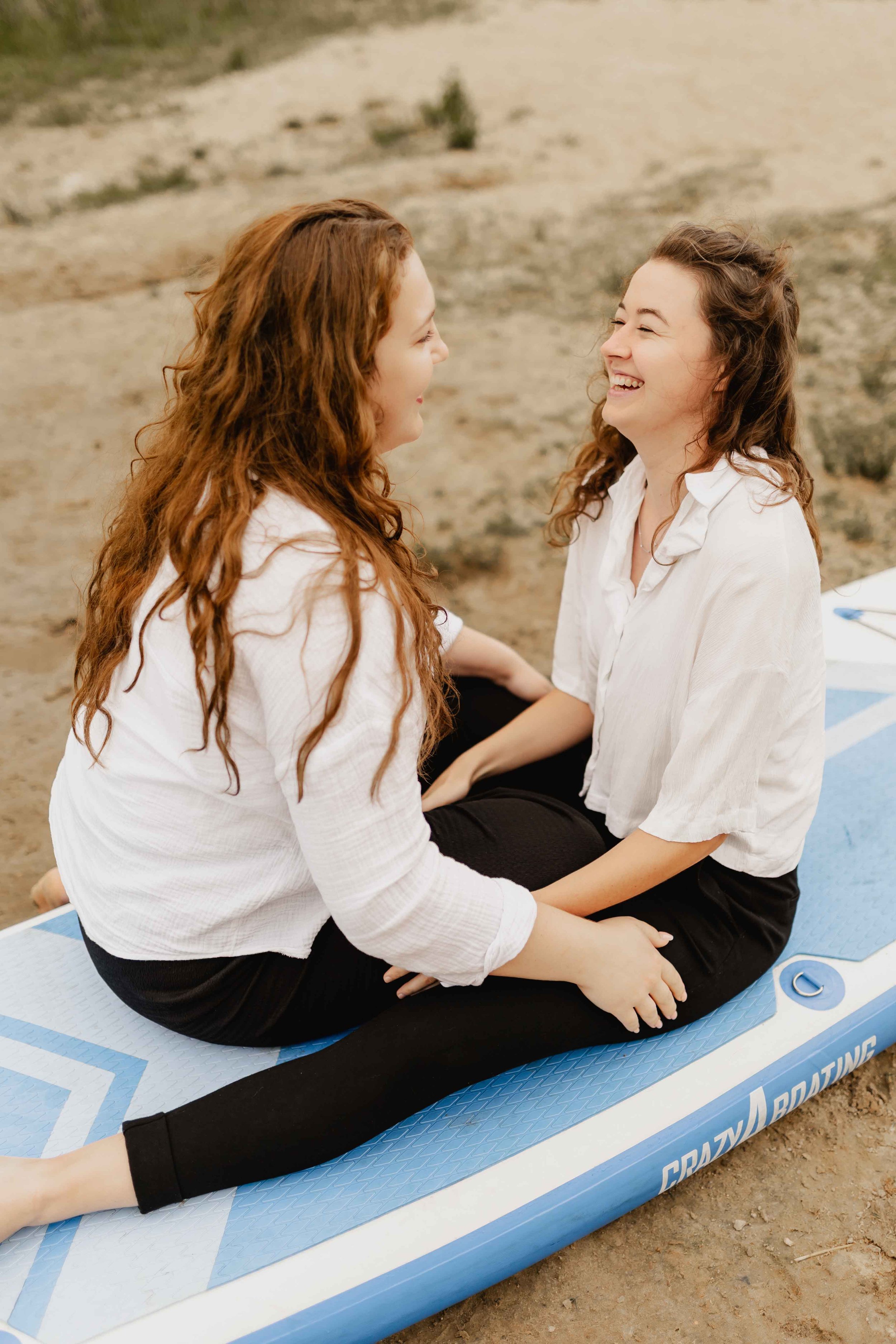 Zwei Frauen sitzen auf einem SUP-Board am Oldenstädter See und schauen sich lächelnd in die Augen