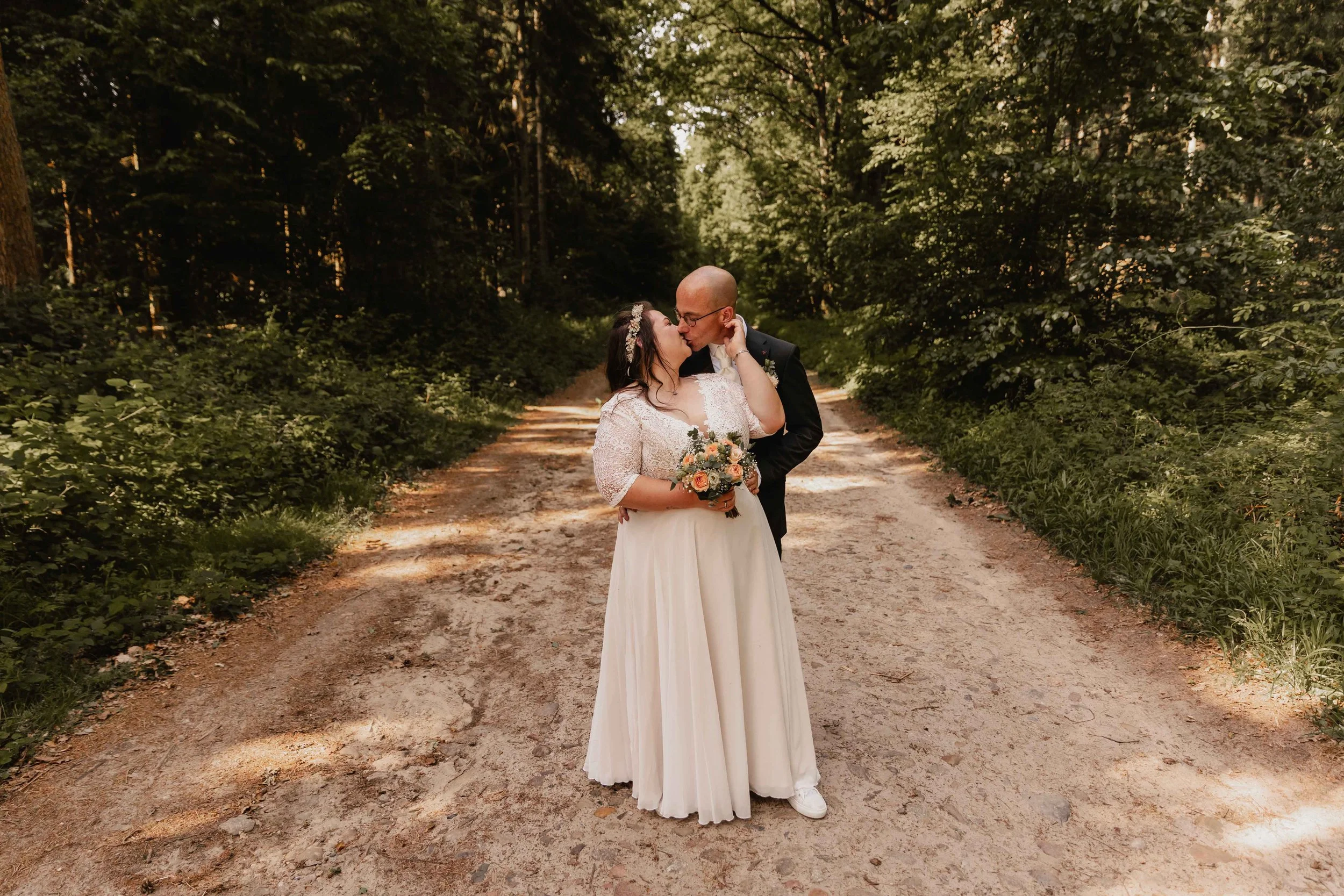Hochzeitspaar steht eng umschlungen auf einem Waldweg und schaut sich verliebt an