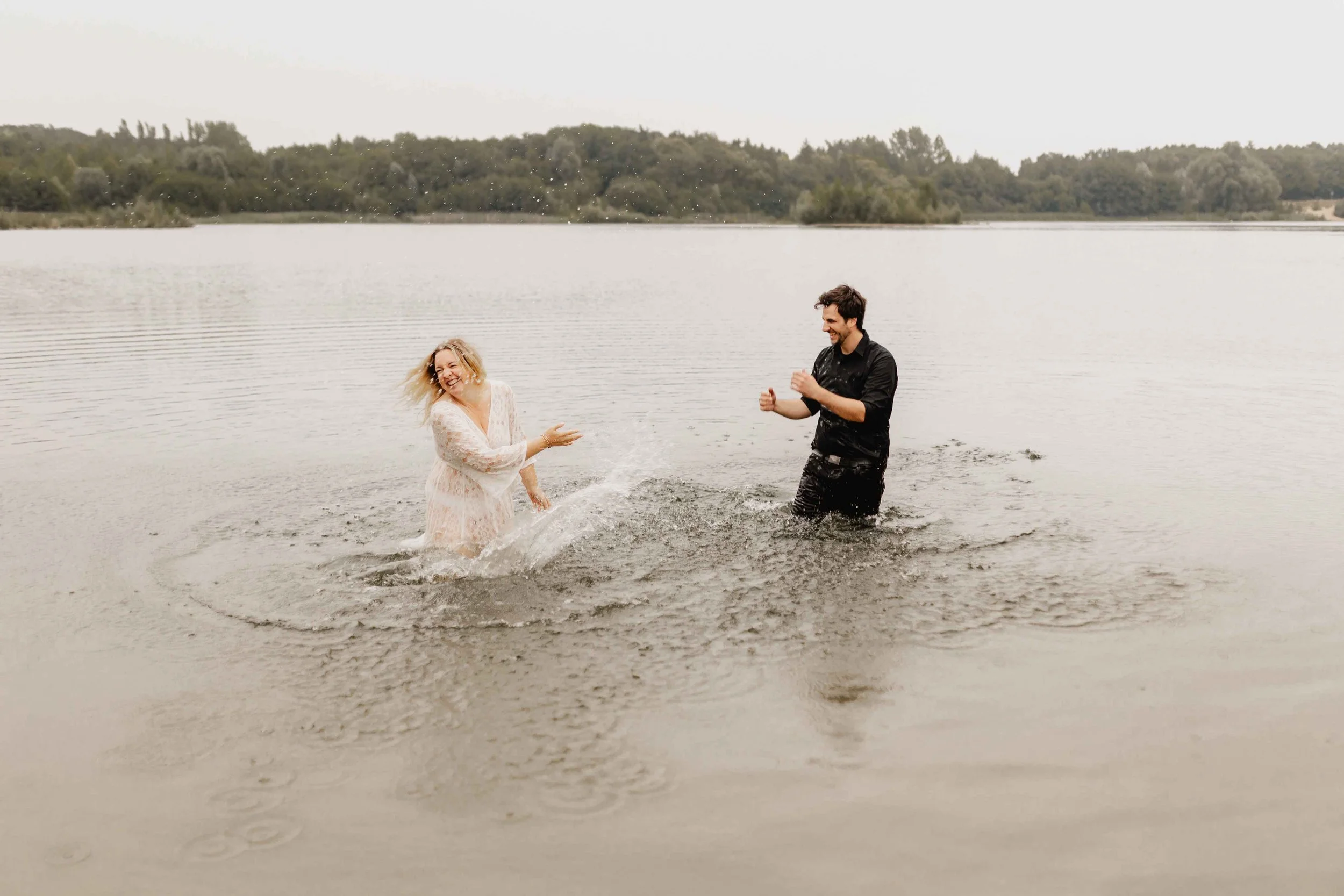 Paar spielt lachend im Wasser und spritzt sich gegenseitig nass