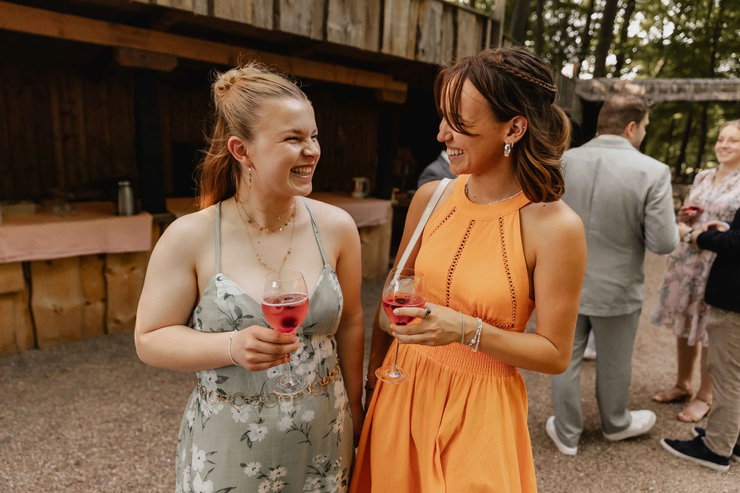 Zwei Freundinnen stoßen mit Roséwein an und lachen herzlich vor der Location