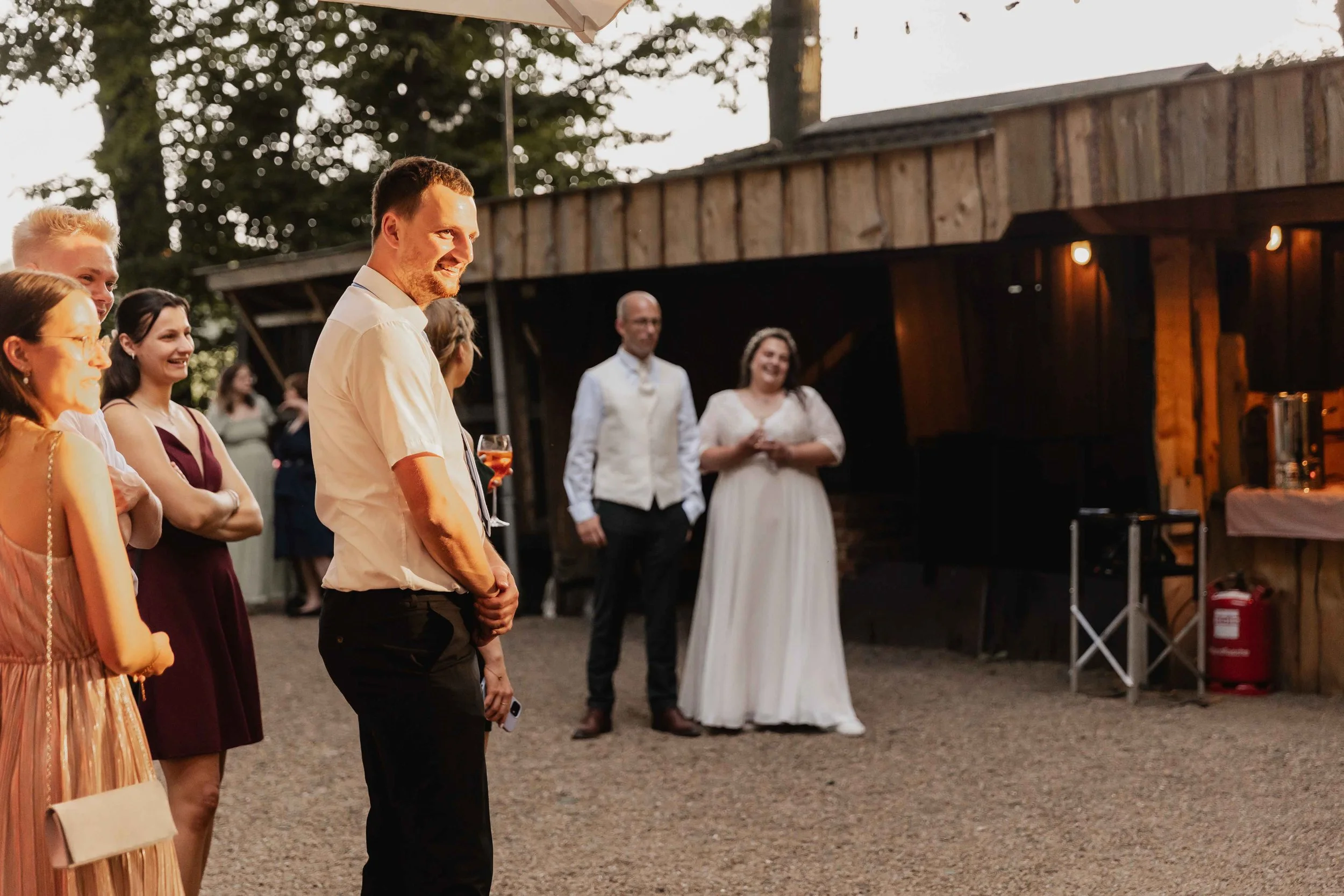 Gäste lachen während einer Hochzeitseinlage bei Sonnenlicht im Innenhof