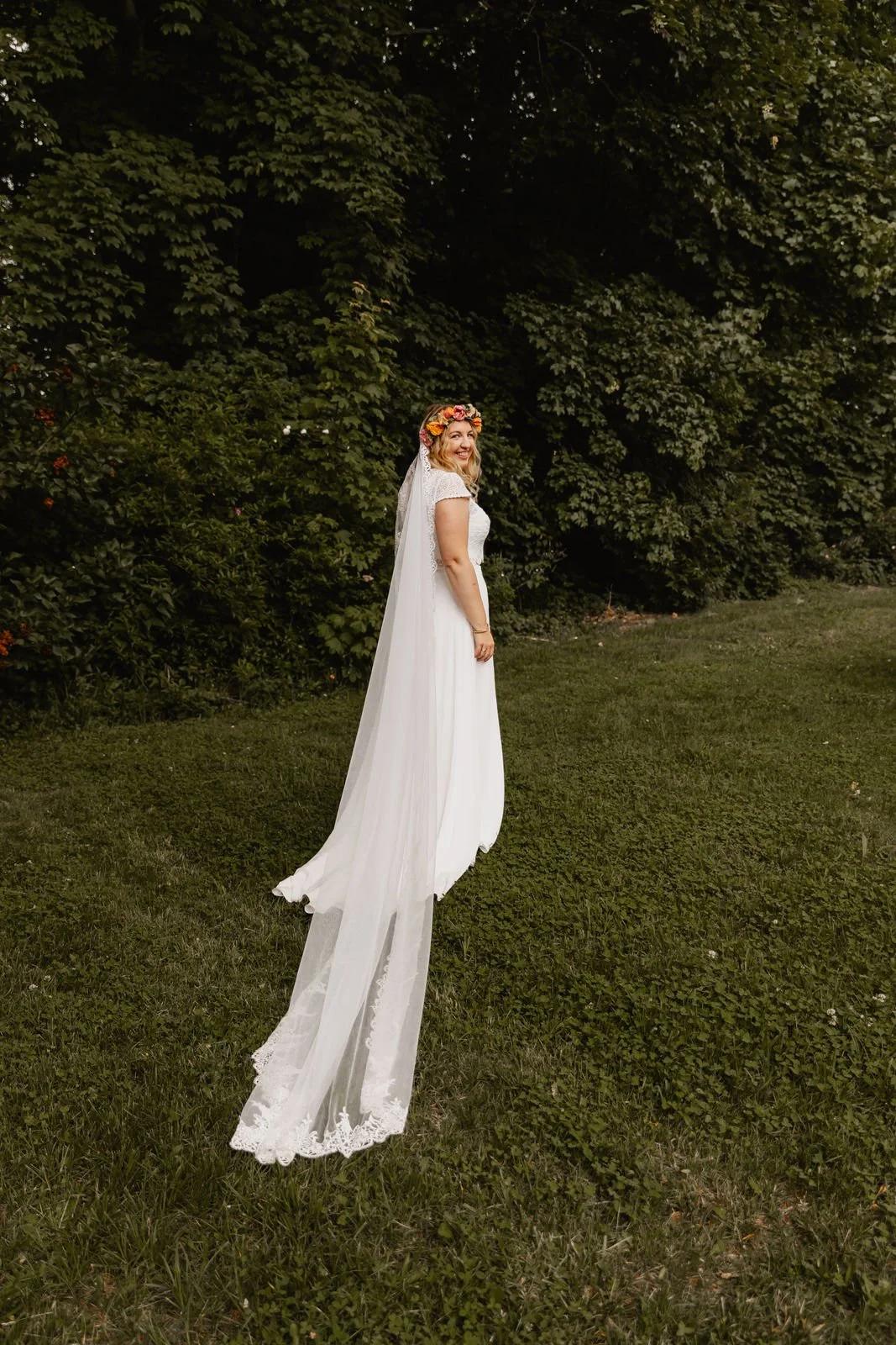 Braut im weißen Hochzeitskleid posiert lächelnd im Grünen während einer Sommerhochzeit in Lüneburg