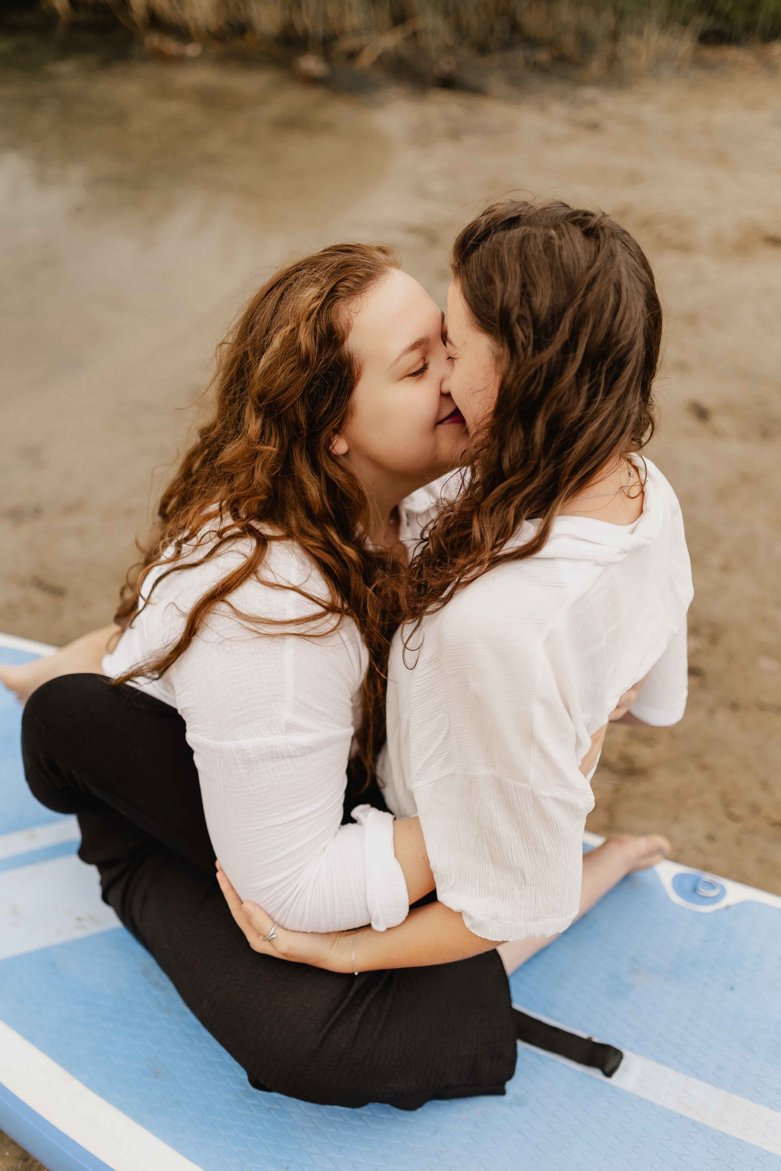 Zwei Frauen sitzen auf einem SUP-Board am Oldenstädter See und küssen sich innig