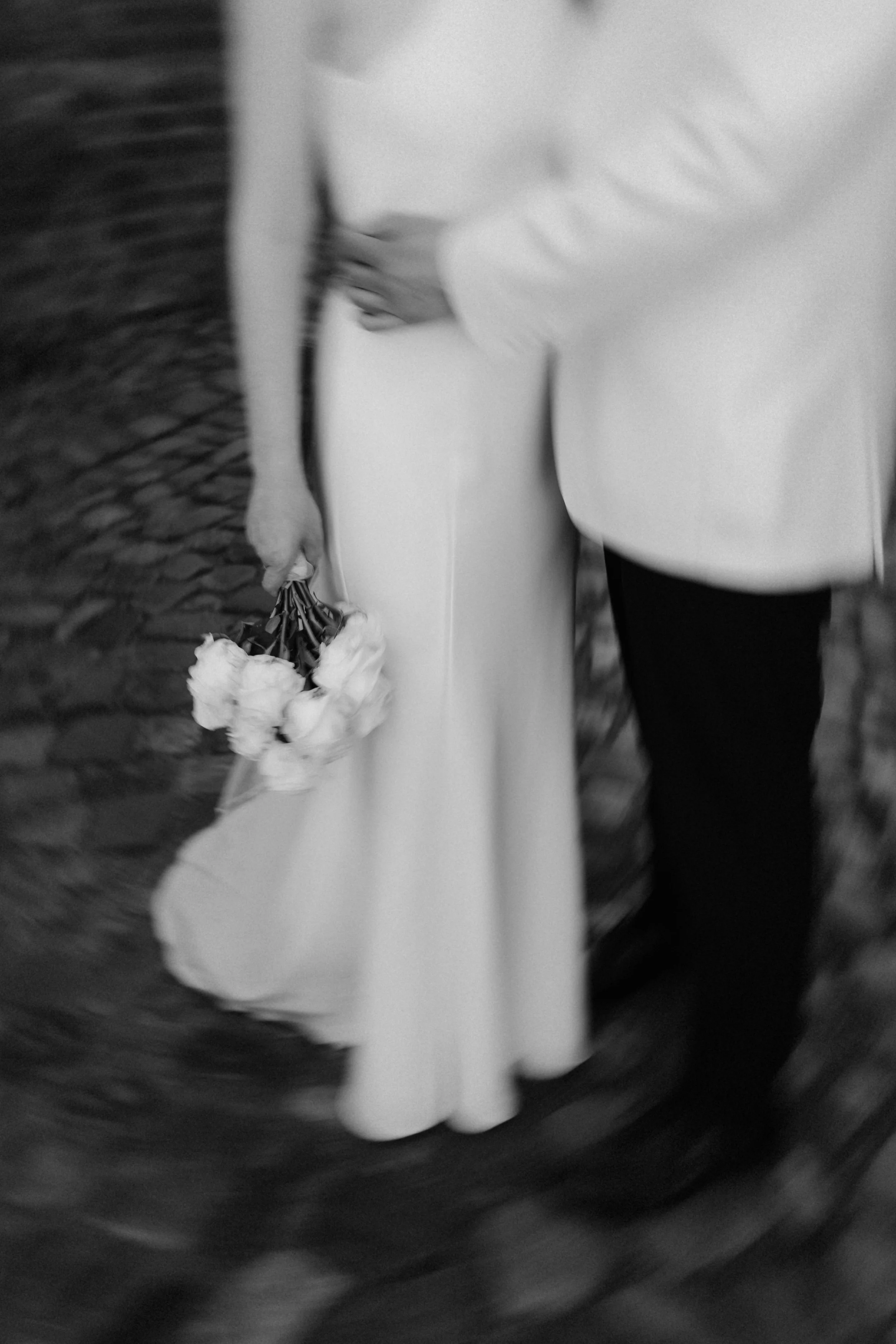 Schwarz-Weiß-Detailaufnahme eines Brautpaares mit Brautstrauß und elegantem Hochzeitsoutfit in Lüneburg.