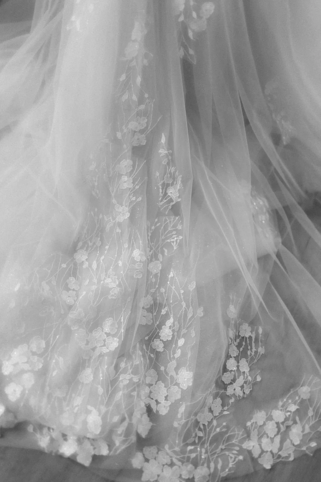 Schwarz-Weiß-Detailaufnahme eines Brautkleides mit feinen floralen Spitzen- und Tüllverzierungen