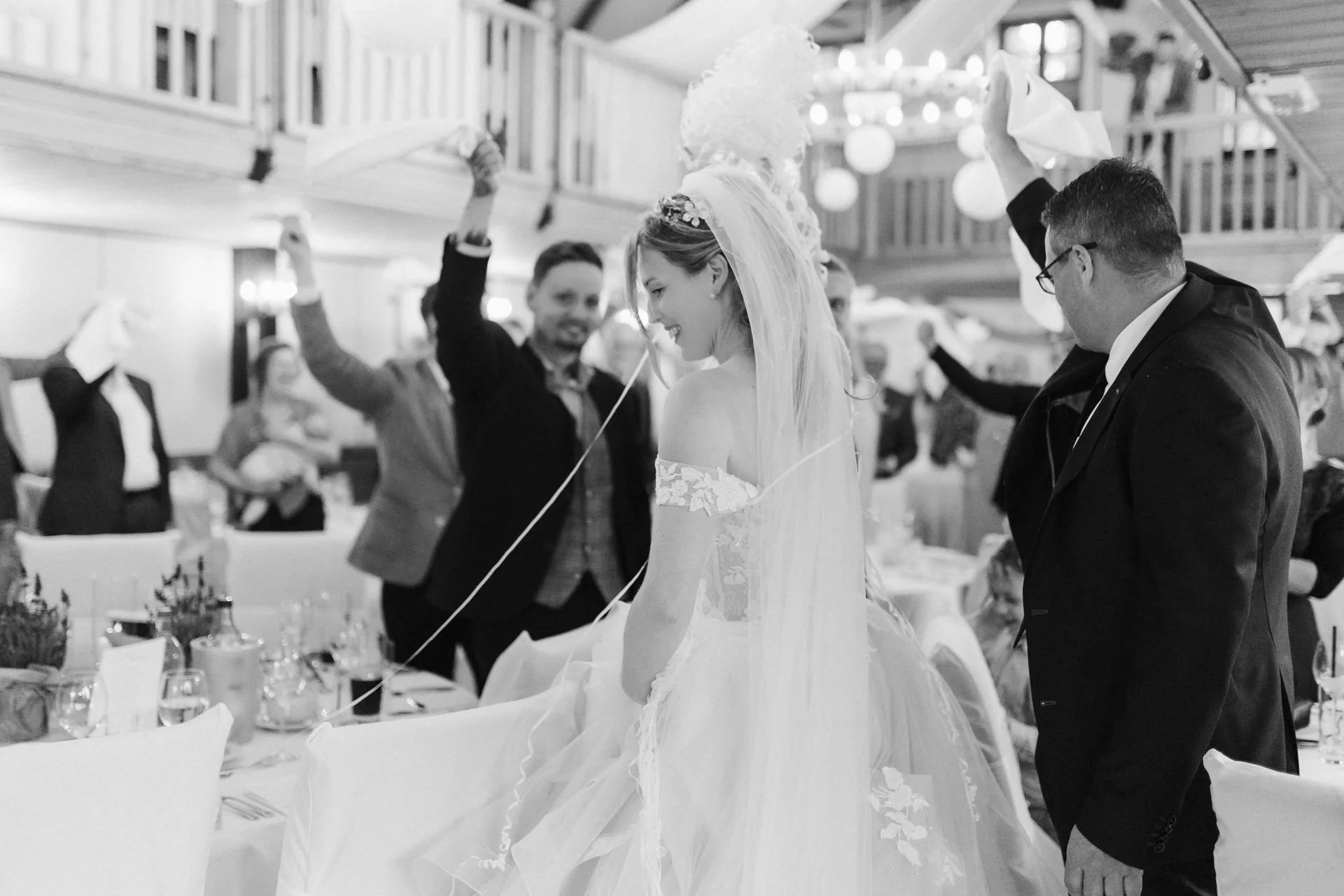 Schwarz-Weiß-Aufnahme der lachenden Braut beim ausgelassenen Hochzeitstanz mit ihren Gästen im festlich dekorierten Heide Hotel Reinstorf bei Lüneburg.