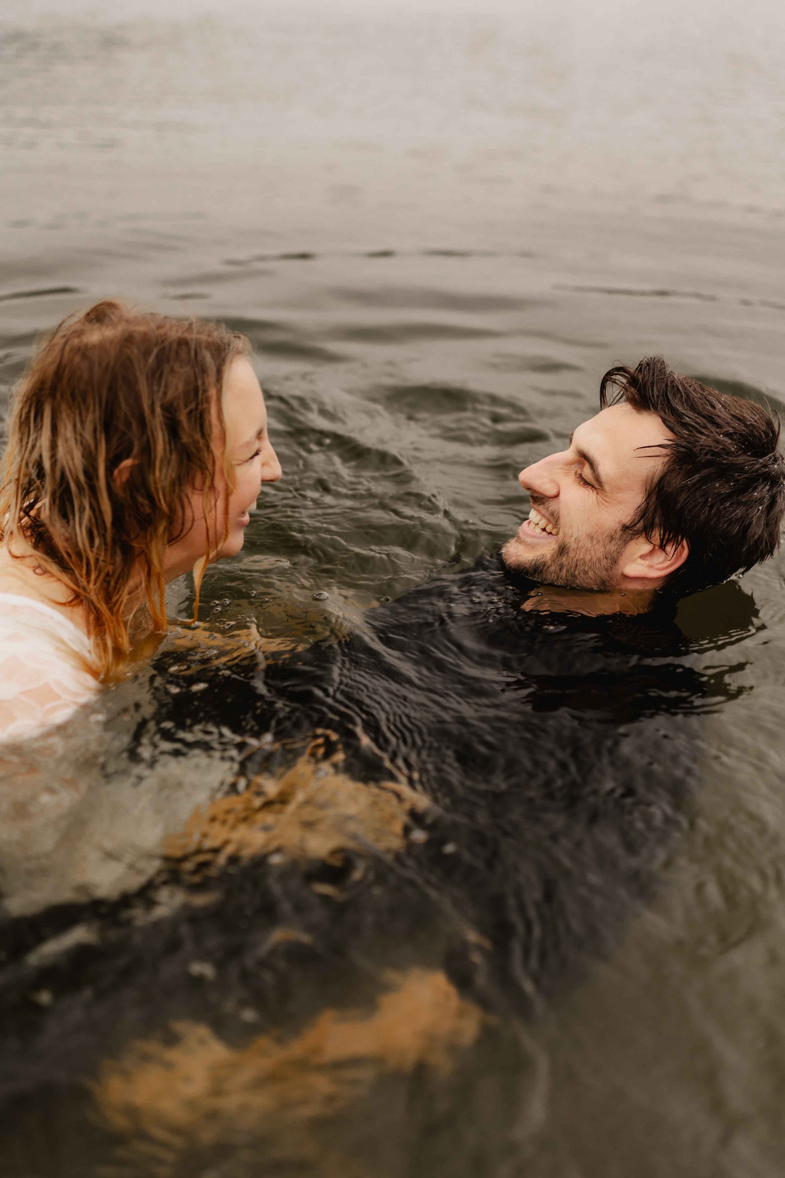 Paar liegt lachend im Wasser und schaut sich spielerisch an