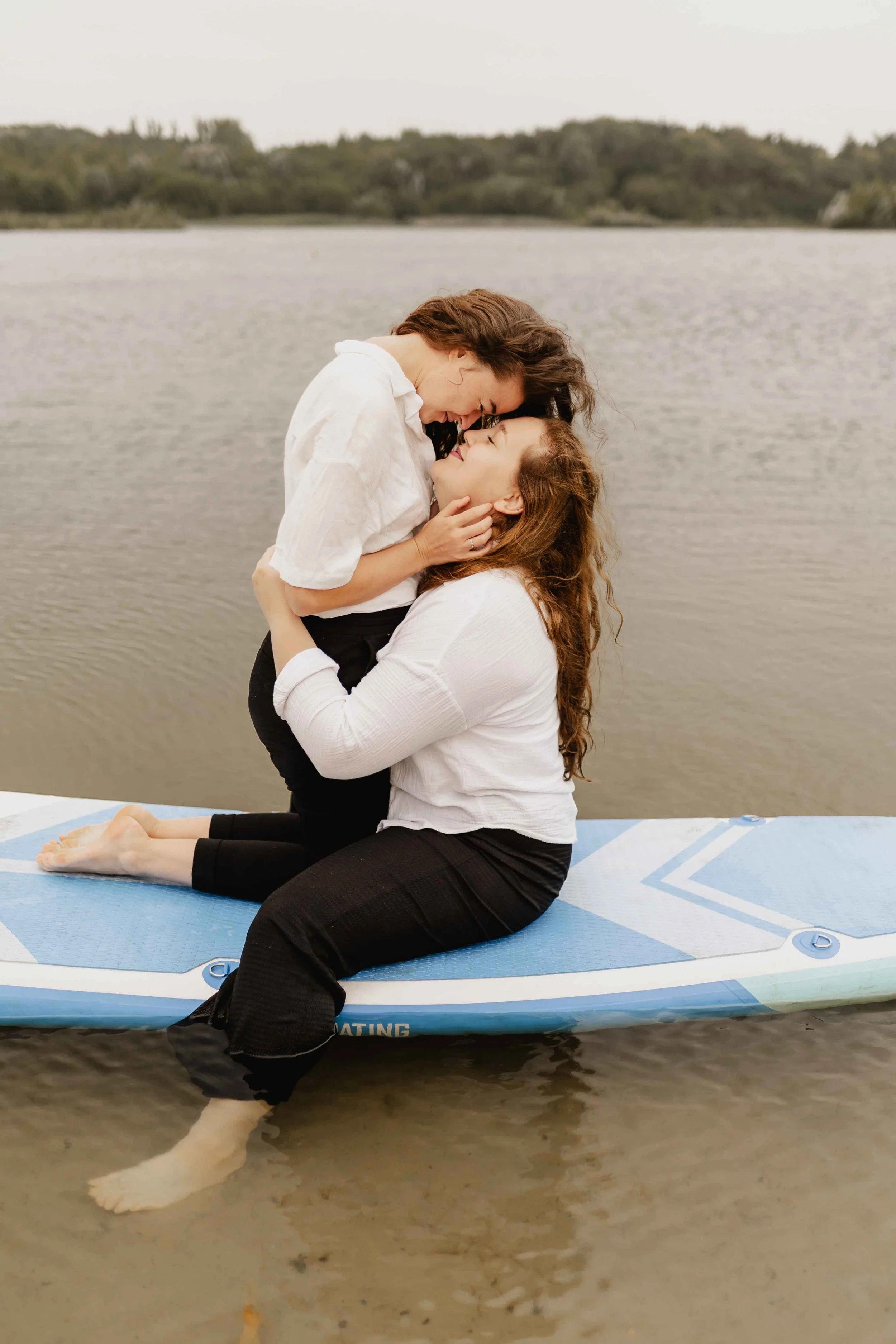 Zwei Frauen küssen sich innig auf einem SUP am See