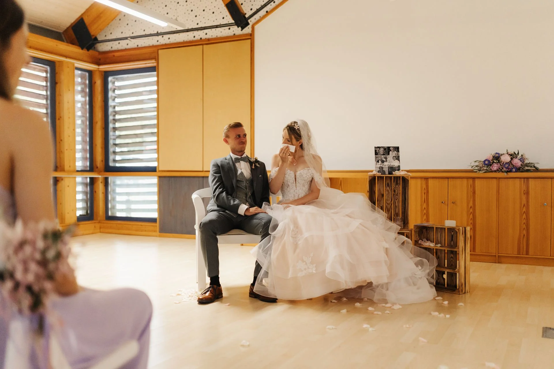 Brautpaar sitzt während der freien Trauung im Heide Hotel Reinstorf bei Lüneburg nebeneinander und tauscht lächelnde Blicke aus – natürliche Hochzeitsreportage einer emotionalen Trauung im Innenbereich.