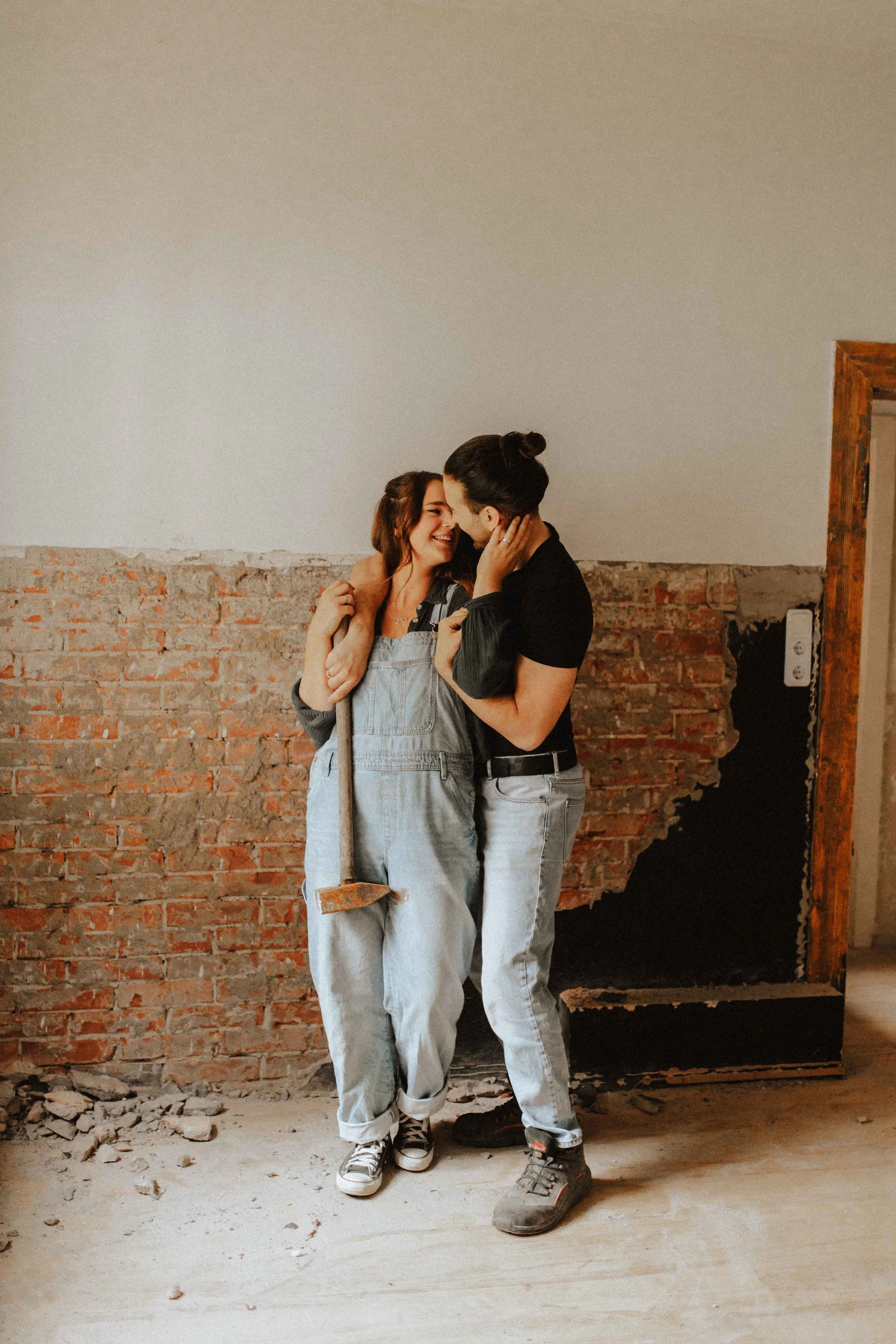 Verliebtes Paarshooting auf Baustelle – Paar lehnt eng an Backsteinwand, romantischer Moment während Renovierungsarbeiten in Lüneburg.