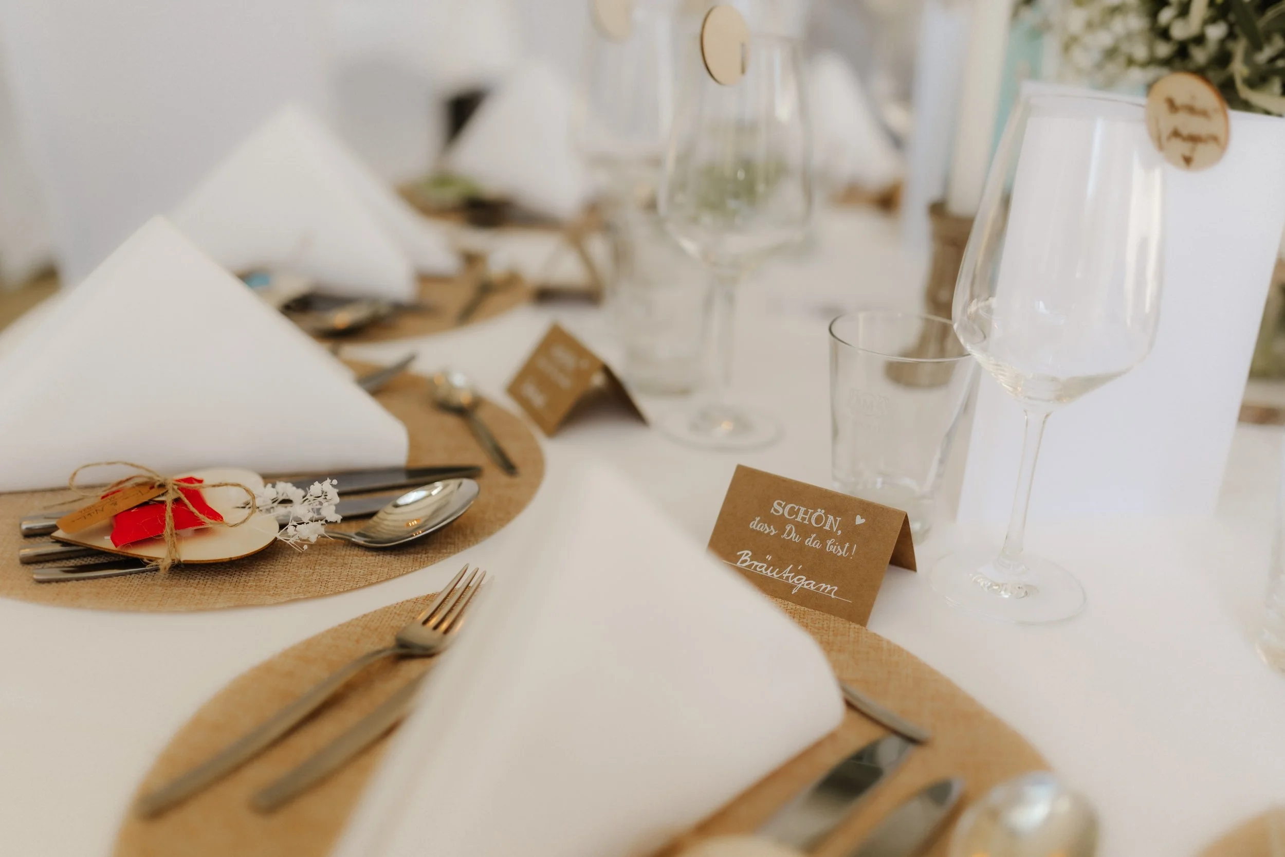 Liebevoll gedeckte Hochzeitstafel mit weißen Stoffservietten, Kraftpapier-Platzsets, Gastgeschenken und kleinen Tischkarten in natürlichem Boho-Stil.