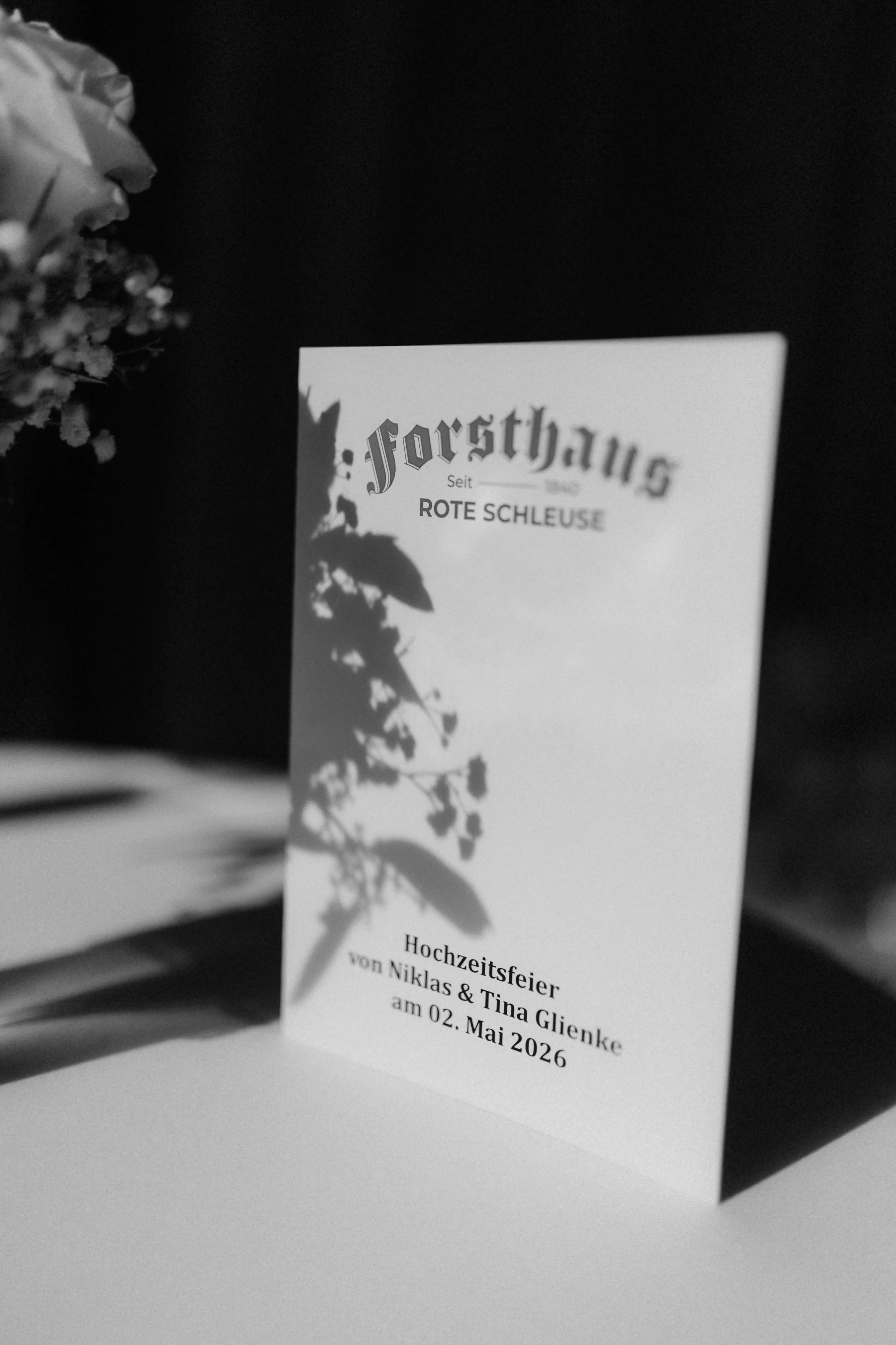 Schwarz-Weiß-Aufnahme eines Aufstellers zur Hochzeitsfeier im Forsthaus Rote Schleuse in Lüneburg mit kunstvollem Schattenwurf von Blättern.