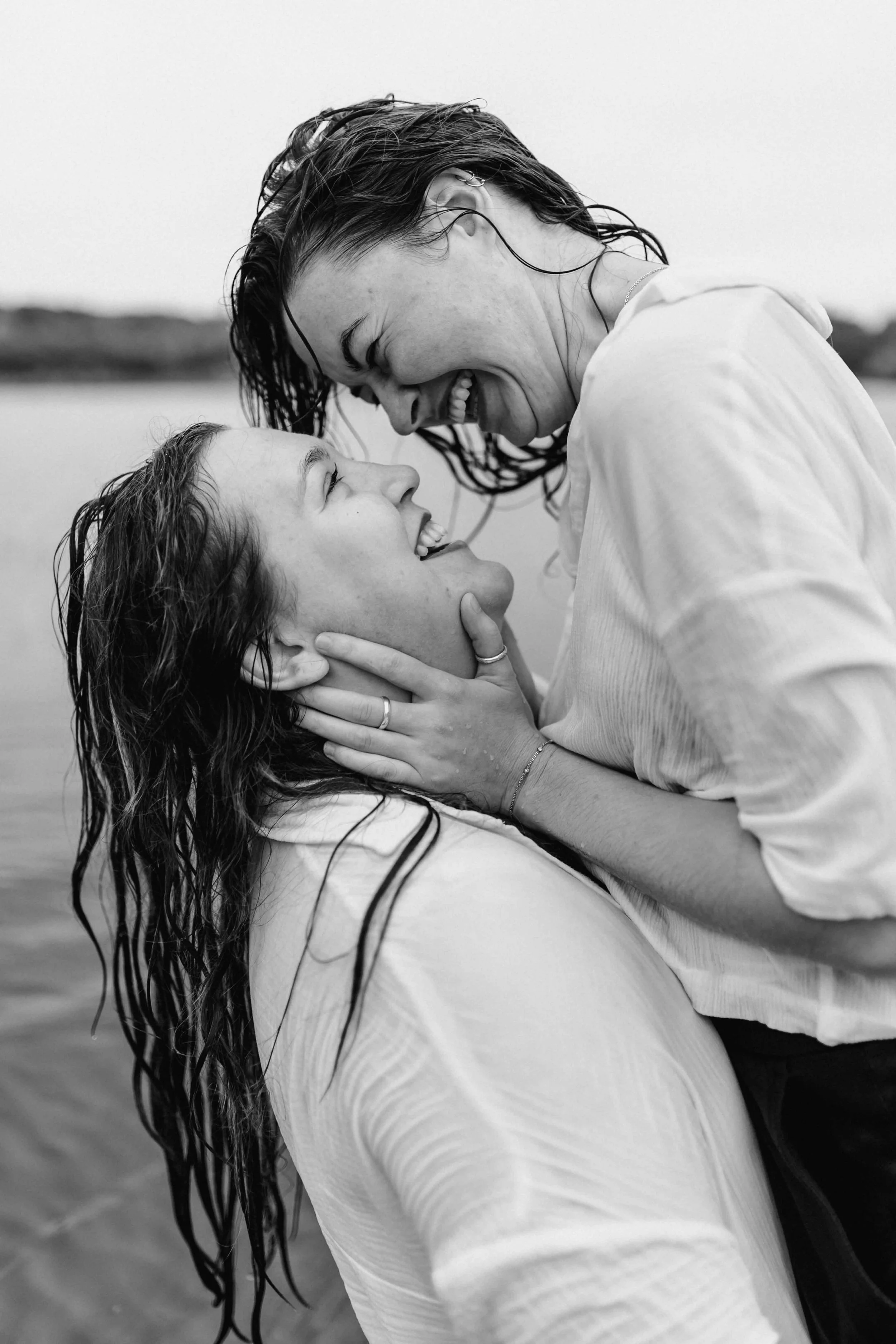 Zwei Frauen lachen verliebt im Wasser und berühren sich kurz vor einem Kuss, Schwarz-Weiß-Fotografie