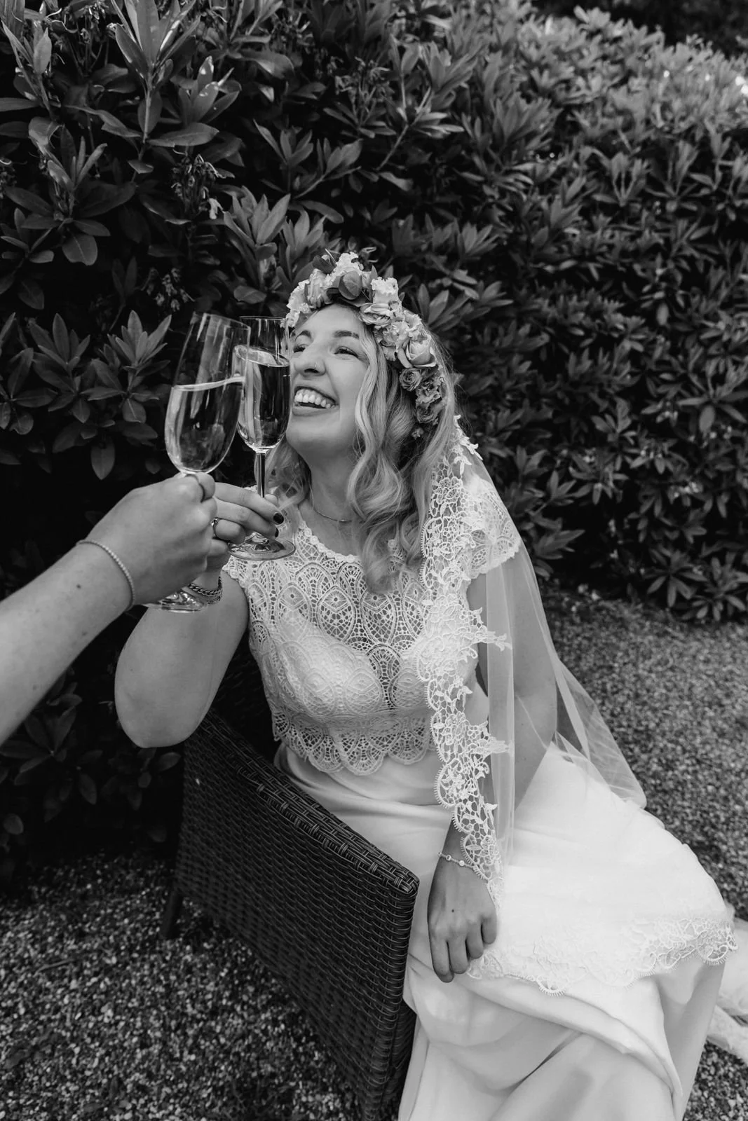 Lachende Braut im Hochzeitskleid stößt mit einem Glas Sekt im Garten in Lüneburg an in schwarz-weiß