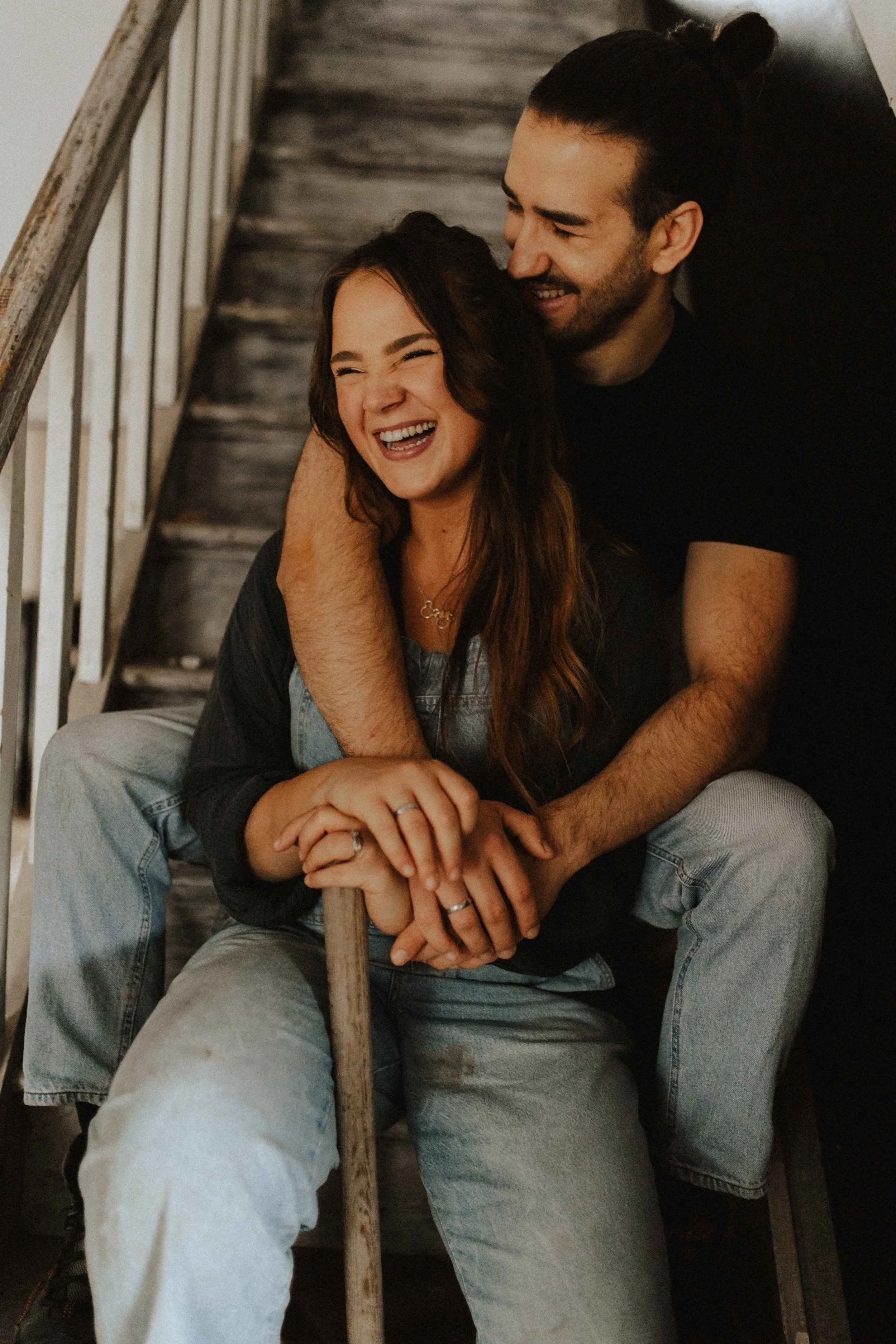 Paarshooting auf Baustelle – lachendes Paar sitzt auf einer Treppe, eng umschlungen, mit gemeinsamem Werkzeug in den Händen in Lüneburg.