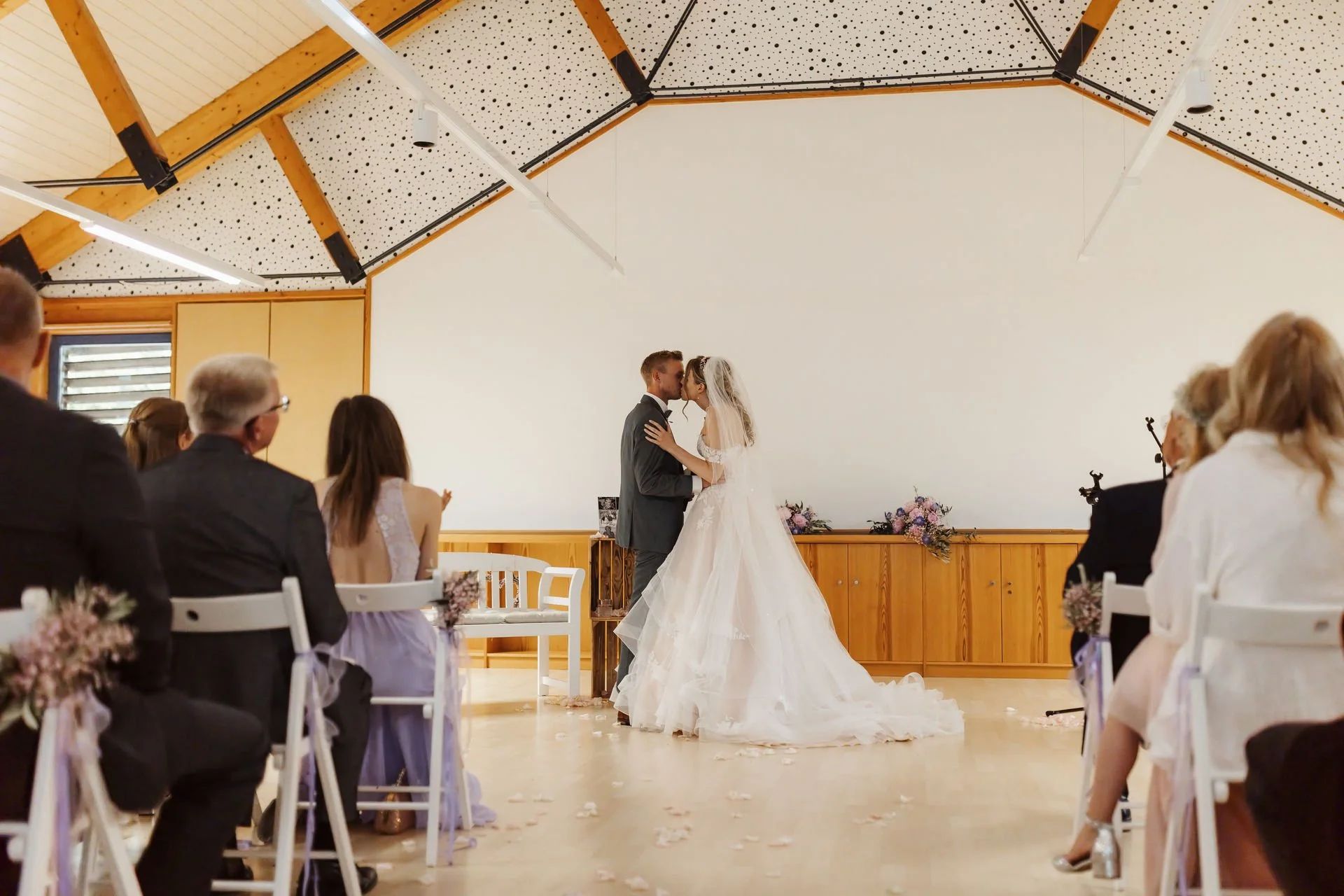 Romantischer Hochzeitskuss nach dem Ja-Wort bei der freien Trauung im Heide Hotel Reinstorf bei Lüneburg. Das Brautpaar küsst sich vor den applaudierenden Hochzeitsgästen.