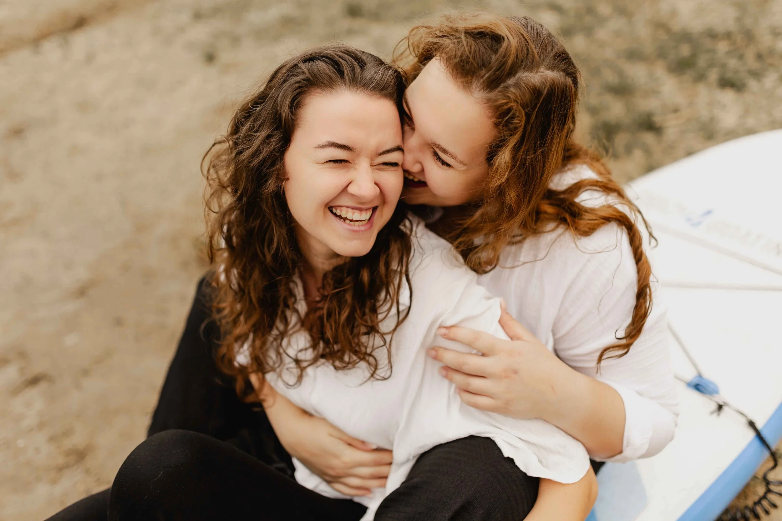 Zwei Frauen sitzen lachend in inniger Umarmung auf einem SUP-Board am Oldenstädter See
