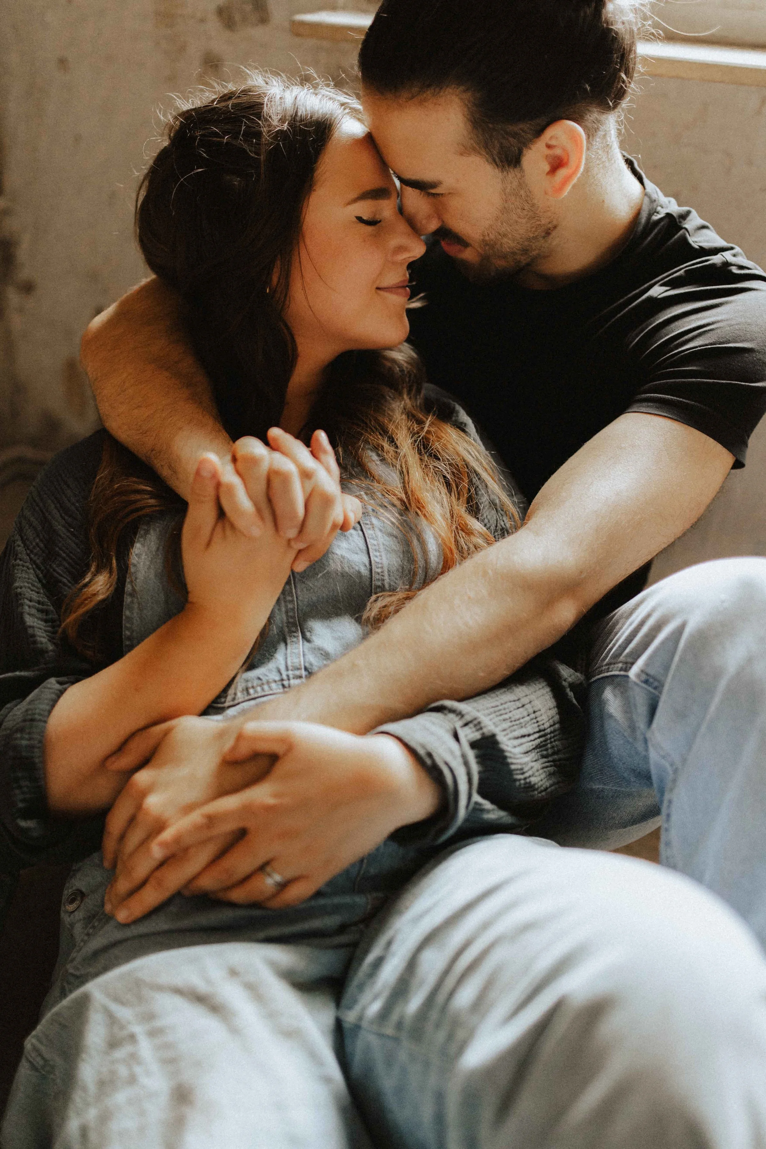 Romantisches Paarshooting in Lüneburg – Mann und Frau sitzen eng umschlungen, Stirn an Stirn, und halten liebevoll ihre Hände, eingefangen in einem intimen Moment voller Nähe.