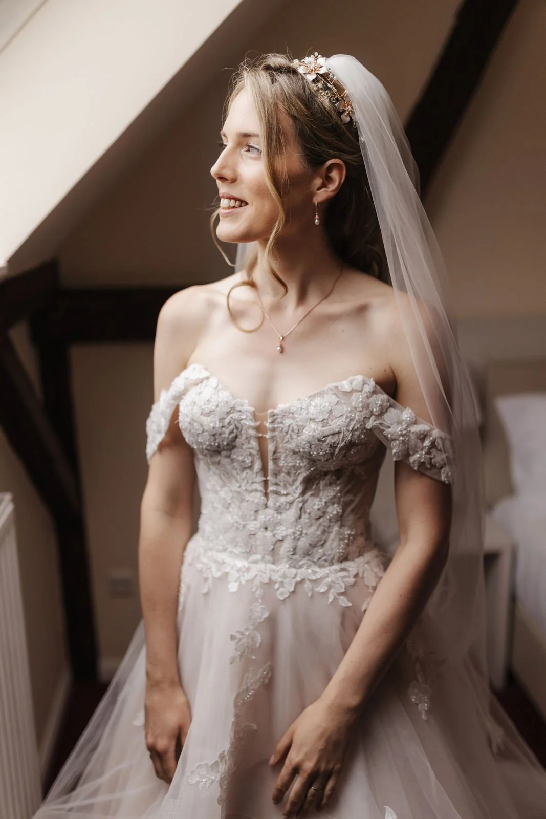 Lächelnde Braut im romantischen Hochzeitskleid mit floraler Spitze, langen Schleier und elegantem Haarschmuck beim Getting Ready im Heide Hotel Reinstorf bei Lüneburg.