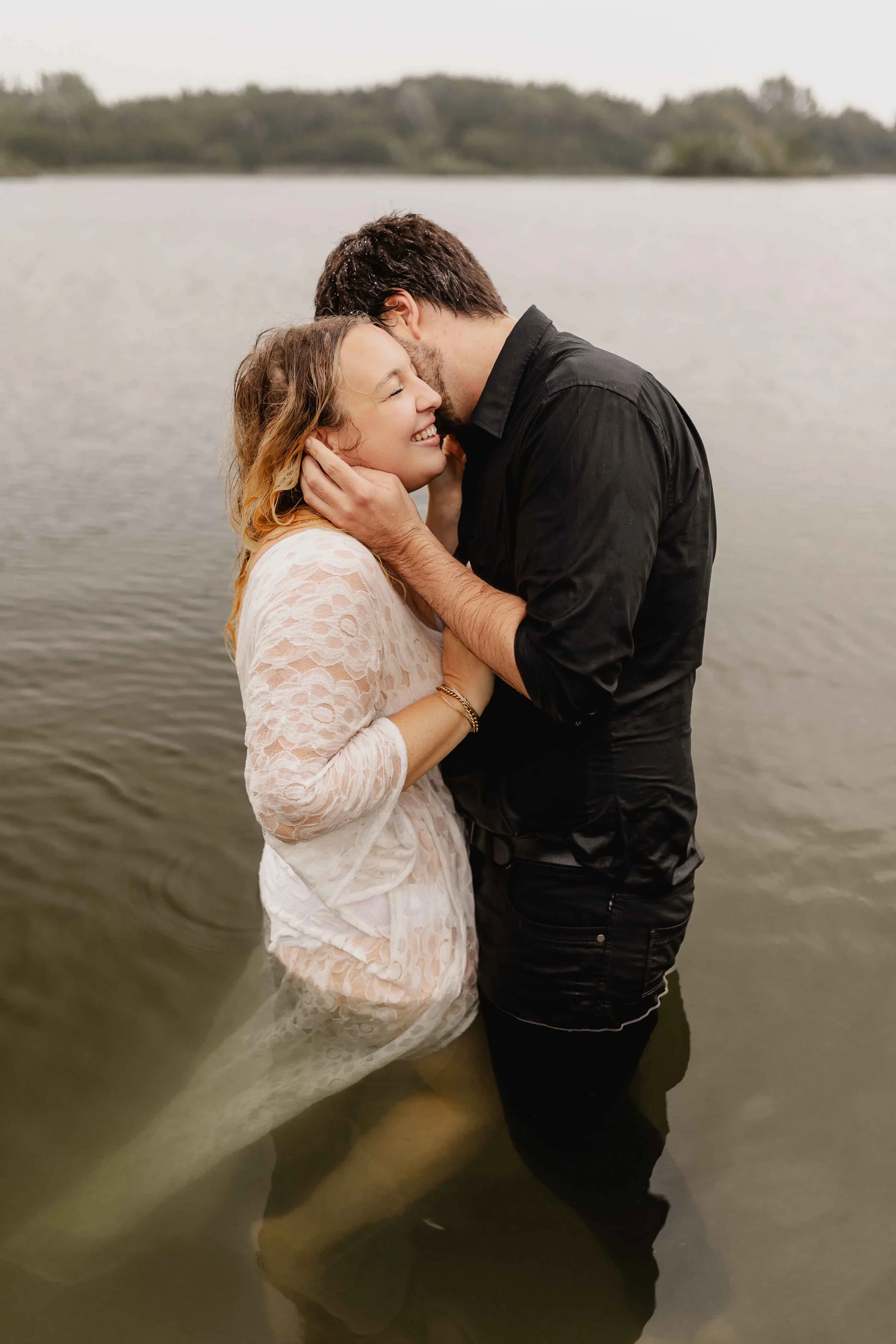 Paar steht im Wasser, hält sich an den Händen und lächelt einander an