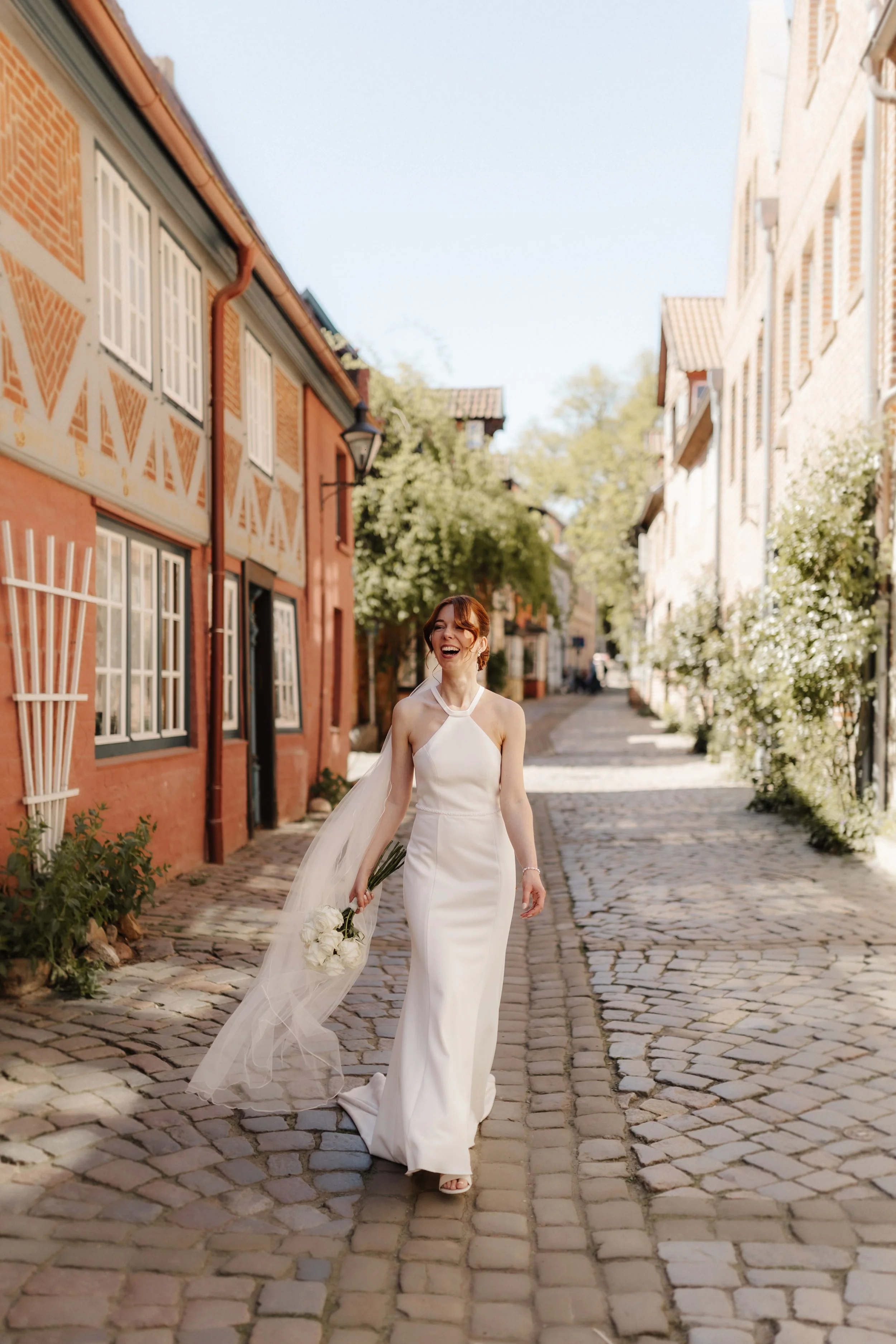 Lachende Braut im modernen Brautkleid beim Spaziergang durch die historische Lüneburger Altstadt.