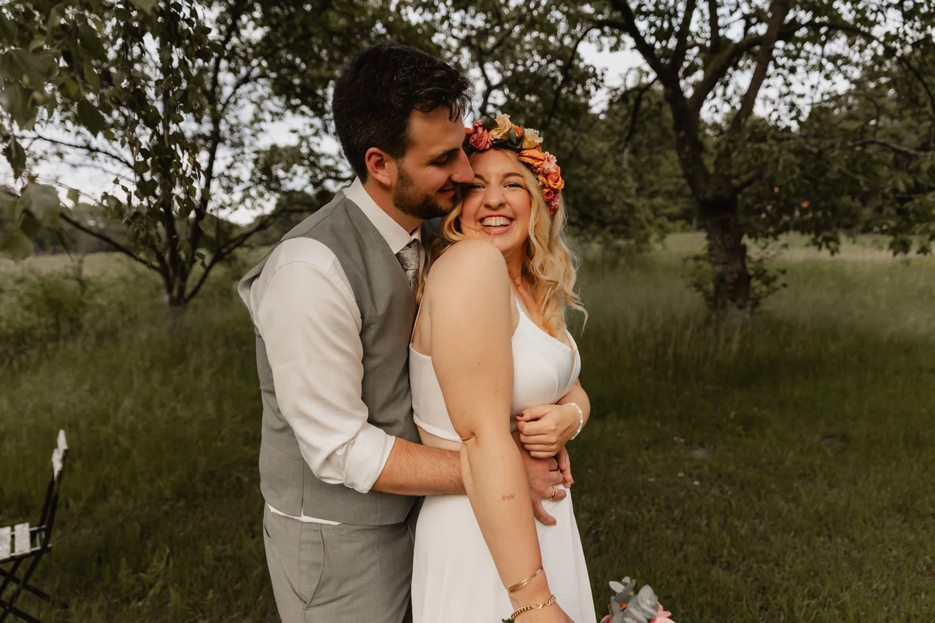 Lachendes Brautpaar umarmt sich bei ihrer Hochzeit im Grünen in Lüneburg