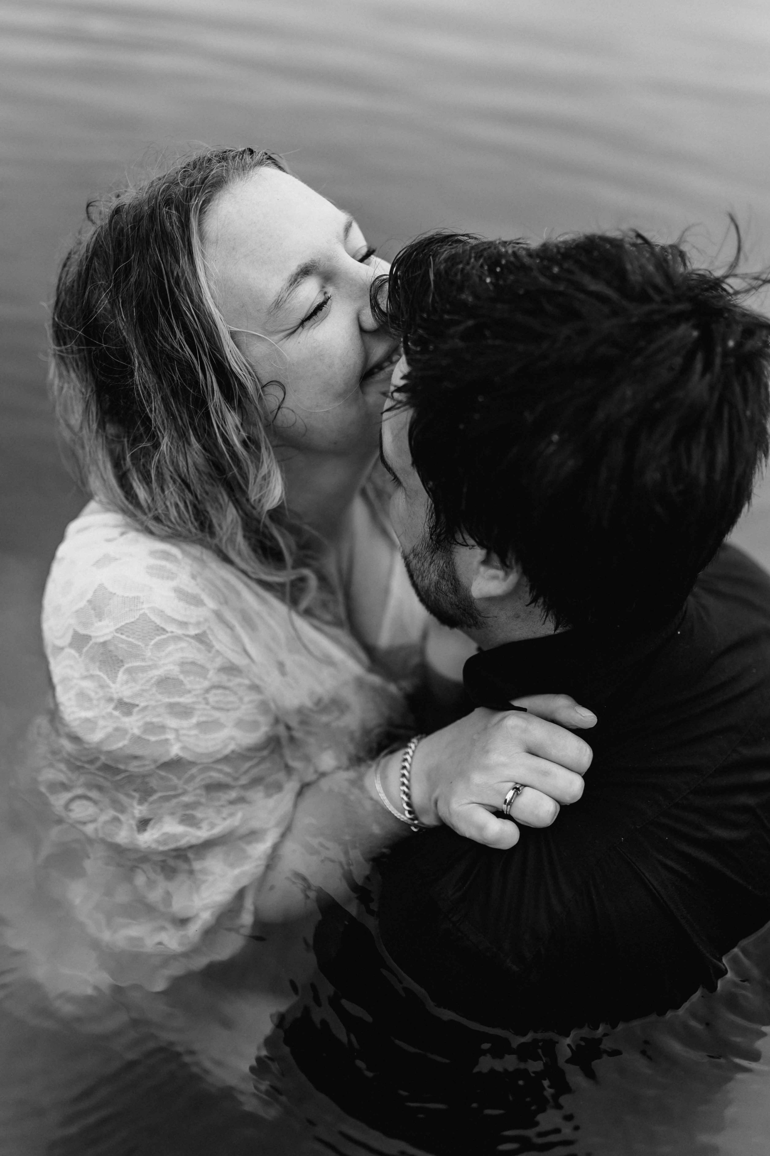 Frau küsst ihren Partner im Wasser lachend auf die Wange