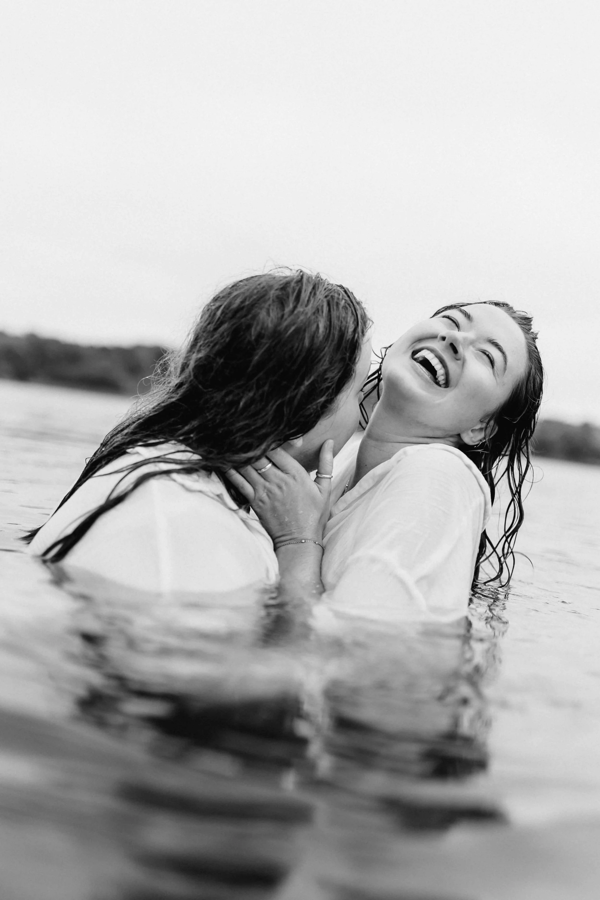 Zwei Frauen umarmen sich im Wasser, eine lacht herzlich, Schwarz-Weiß-Fotografie