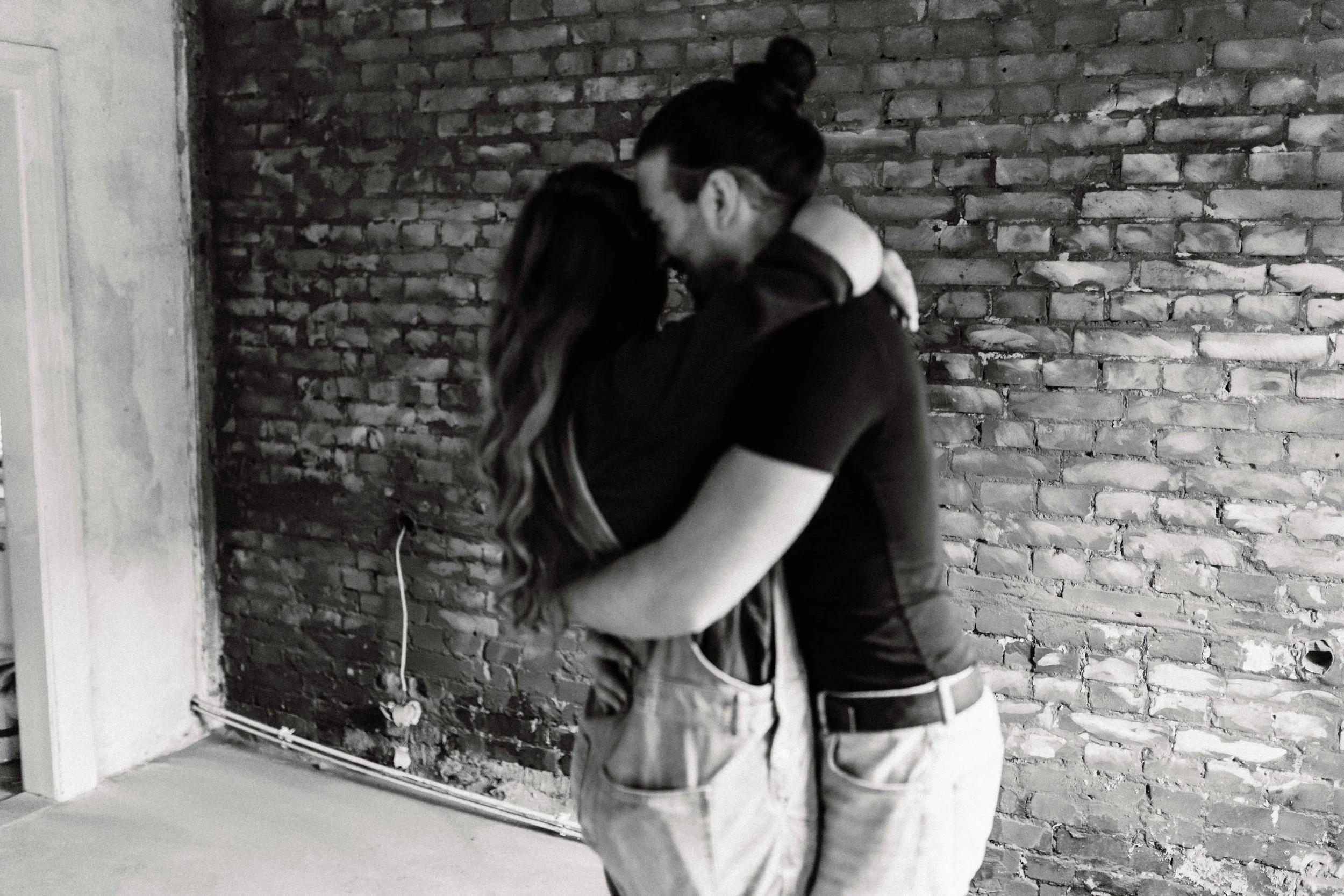 Emotionales Paarshooting in Uelzen – innige Umarmung eines Paares vor einer Backsteinwand in Schwarz-Weiß.