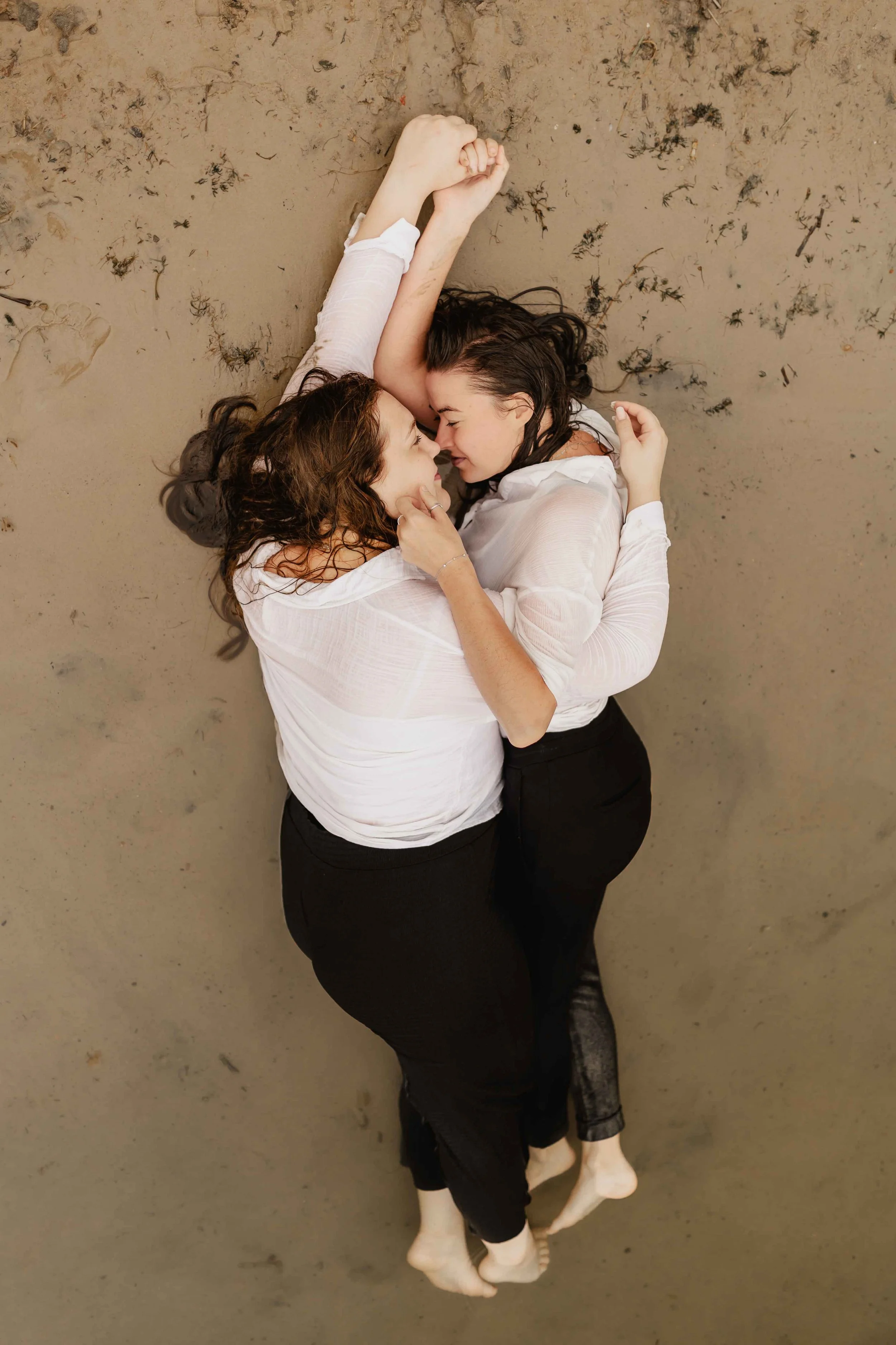 Zwei Frauen liegen eng umschlungen am Sandstrand