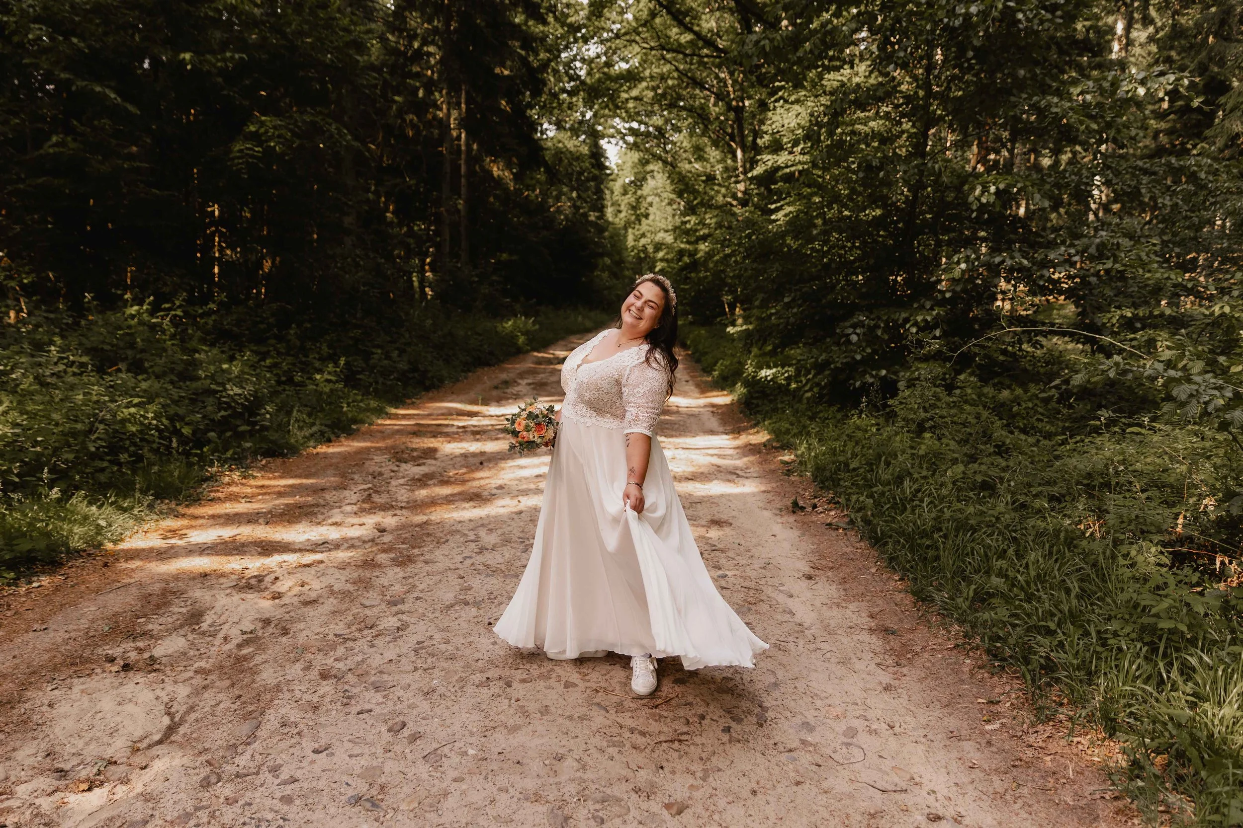 Braut lächelt glücklich mit fließendem Brautkleid mitten im Wald