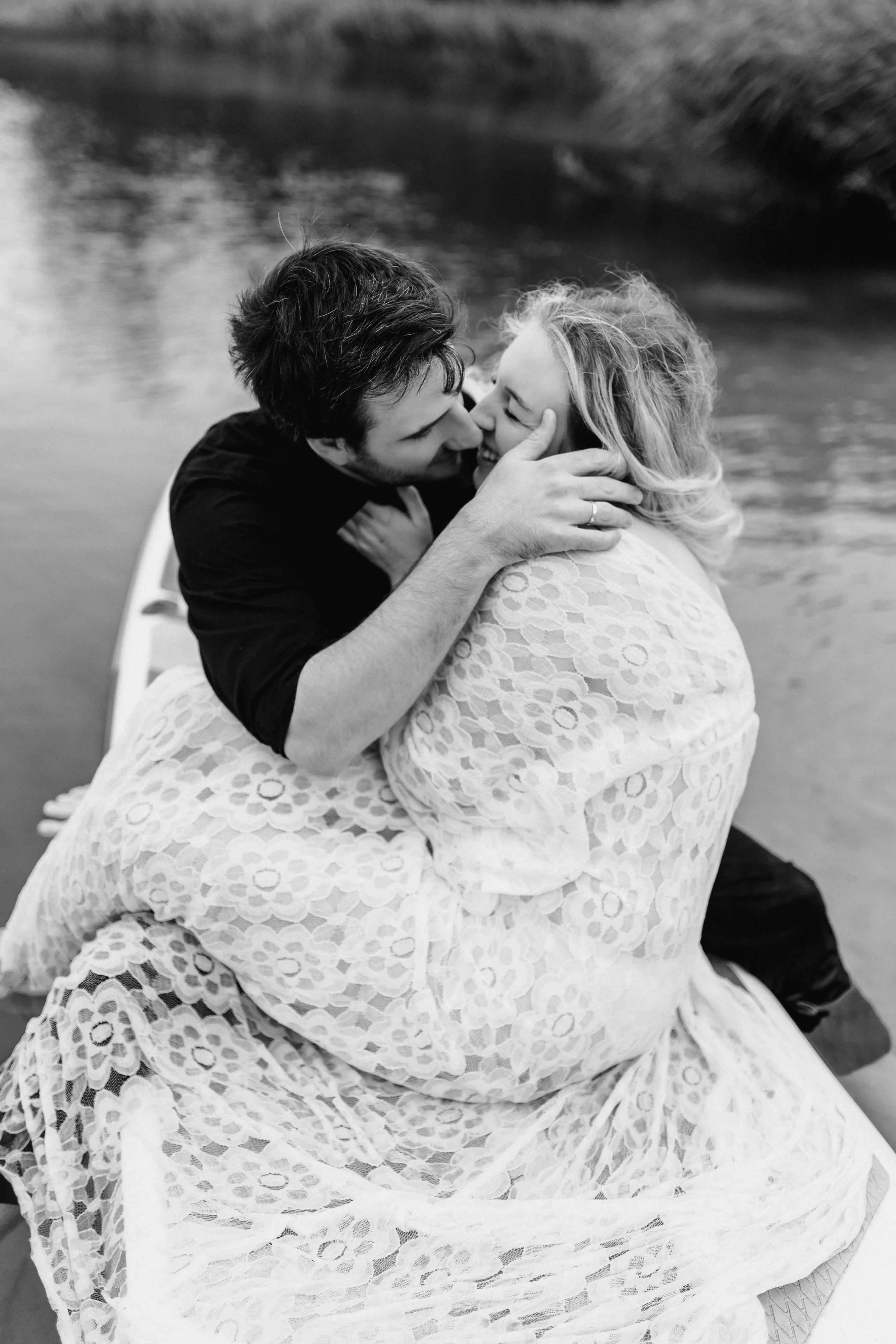 Paar sitzt eingekuschelt in einem Kleid auf dem SUP-Board und küsst sich am See in Schwarz-Weiß