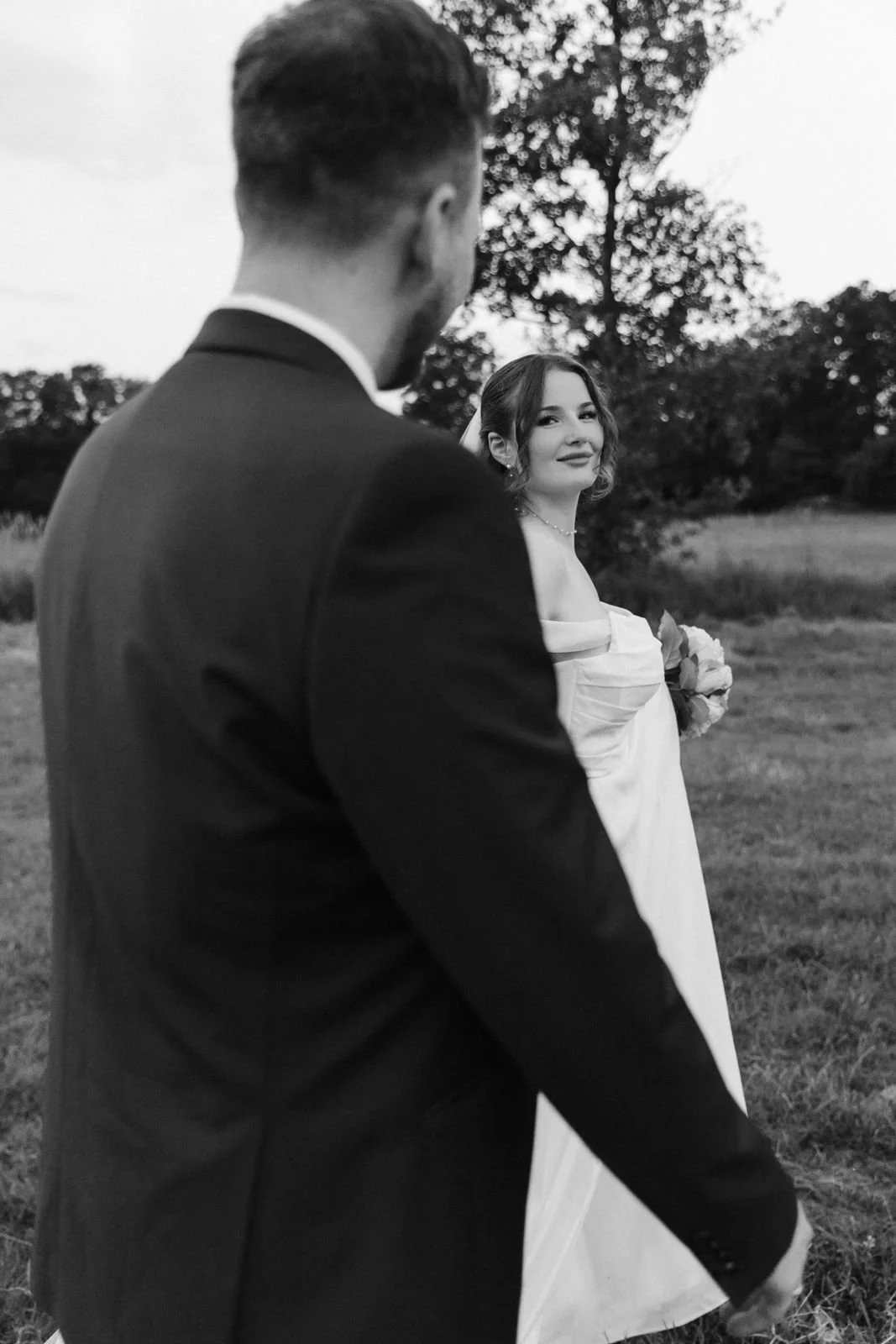 Brautpaar läuft Hand in Hand über eine Wiese und blickt sich dabei an – natürliche Hochzeitsfotografie in Schwarz-Weiß